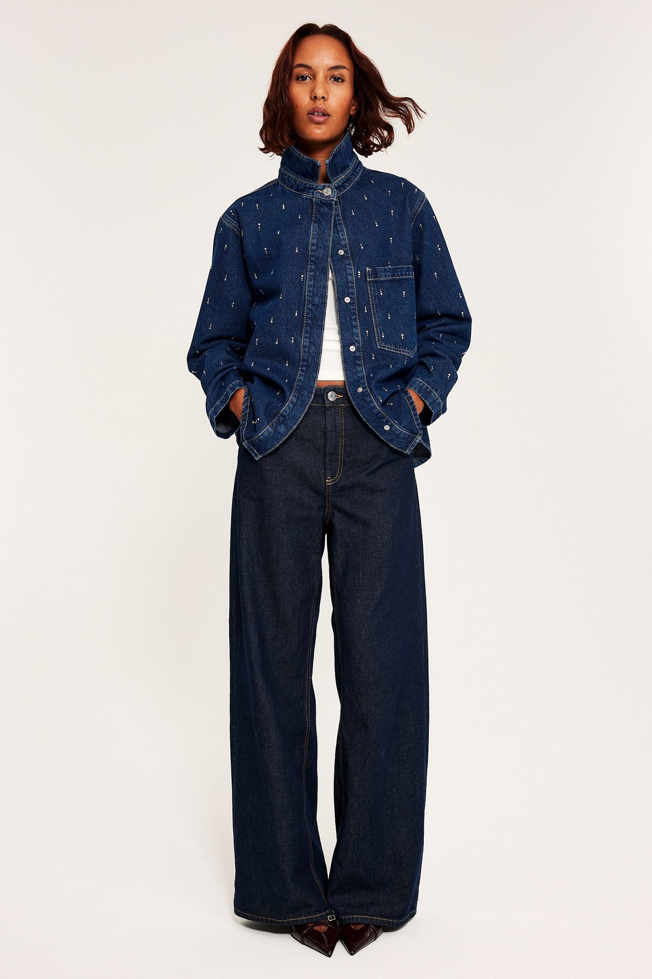 Kvinnlig person visar en denimskjorta med glitterdetaljer, längst upp i bild.