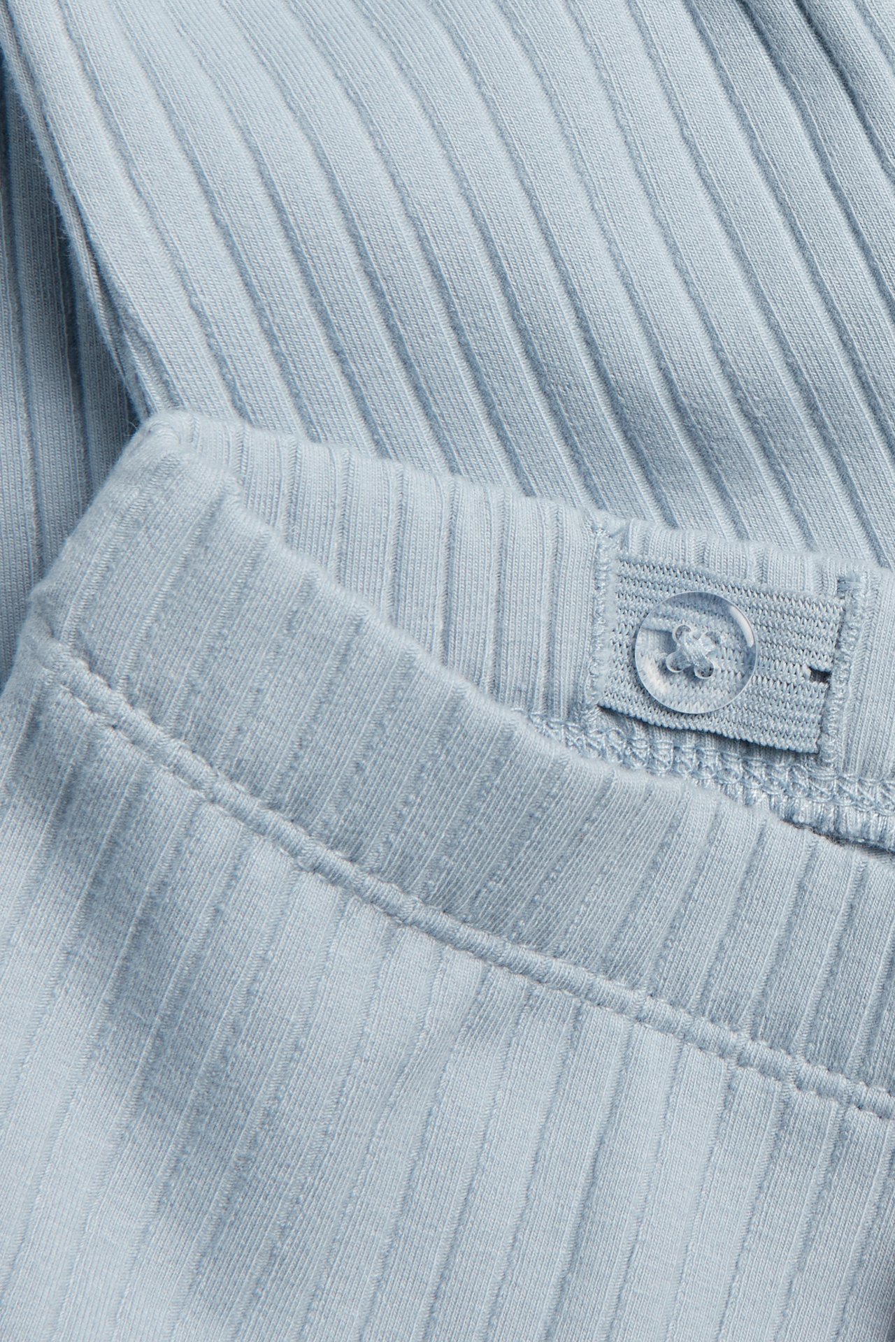 Lähikuva vaaleansinisistä ribatusta leggingseistä, joissa säädettävä joustovyötärö ja läpinäkyvä nappi.