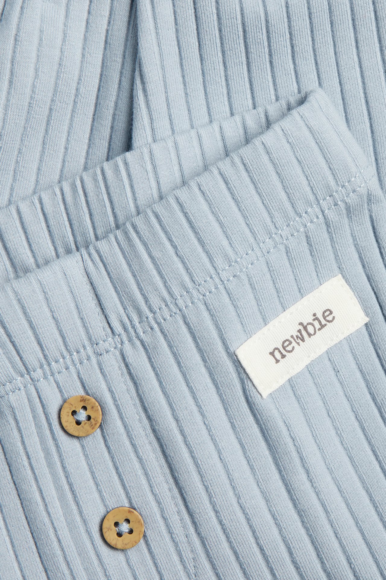 Nærbilde av lys blå ribbestrikkede leggings med to dekorative treknapper og en liten hvit etikett.