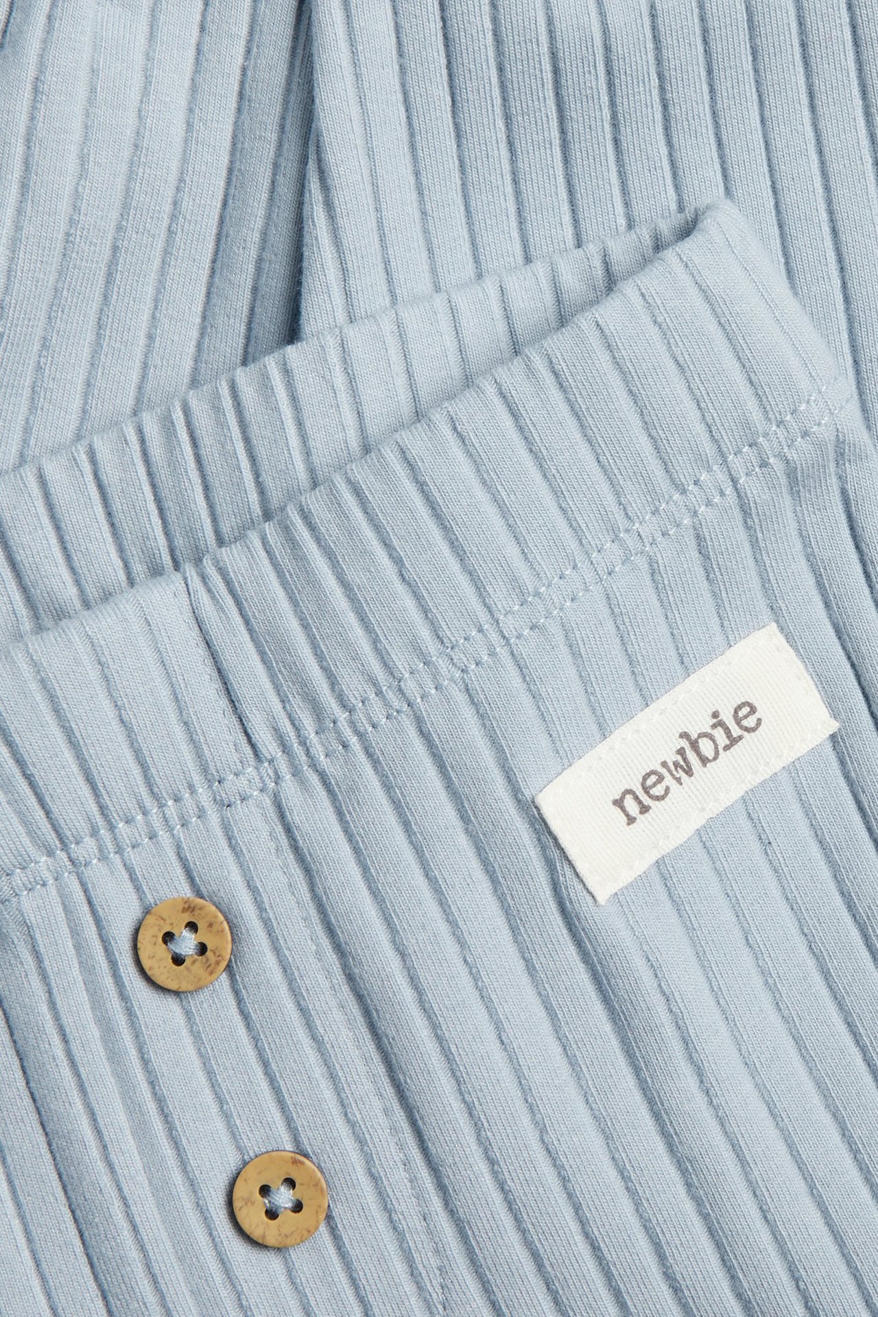 Nærbilde av lys blå ribbestrikkede leggings med to dekorative treknapper og en liten hvit etikett.