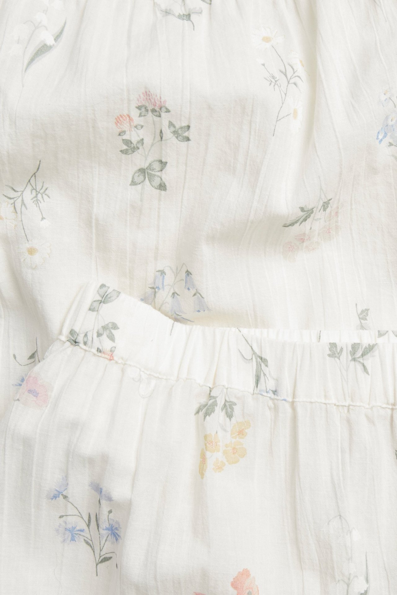 Zbliżenie na kremową piżamową tkaninę bawełnianą z delikatnym kwiatowym wzorem i falbanką.