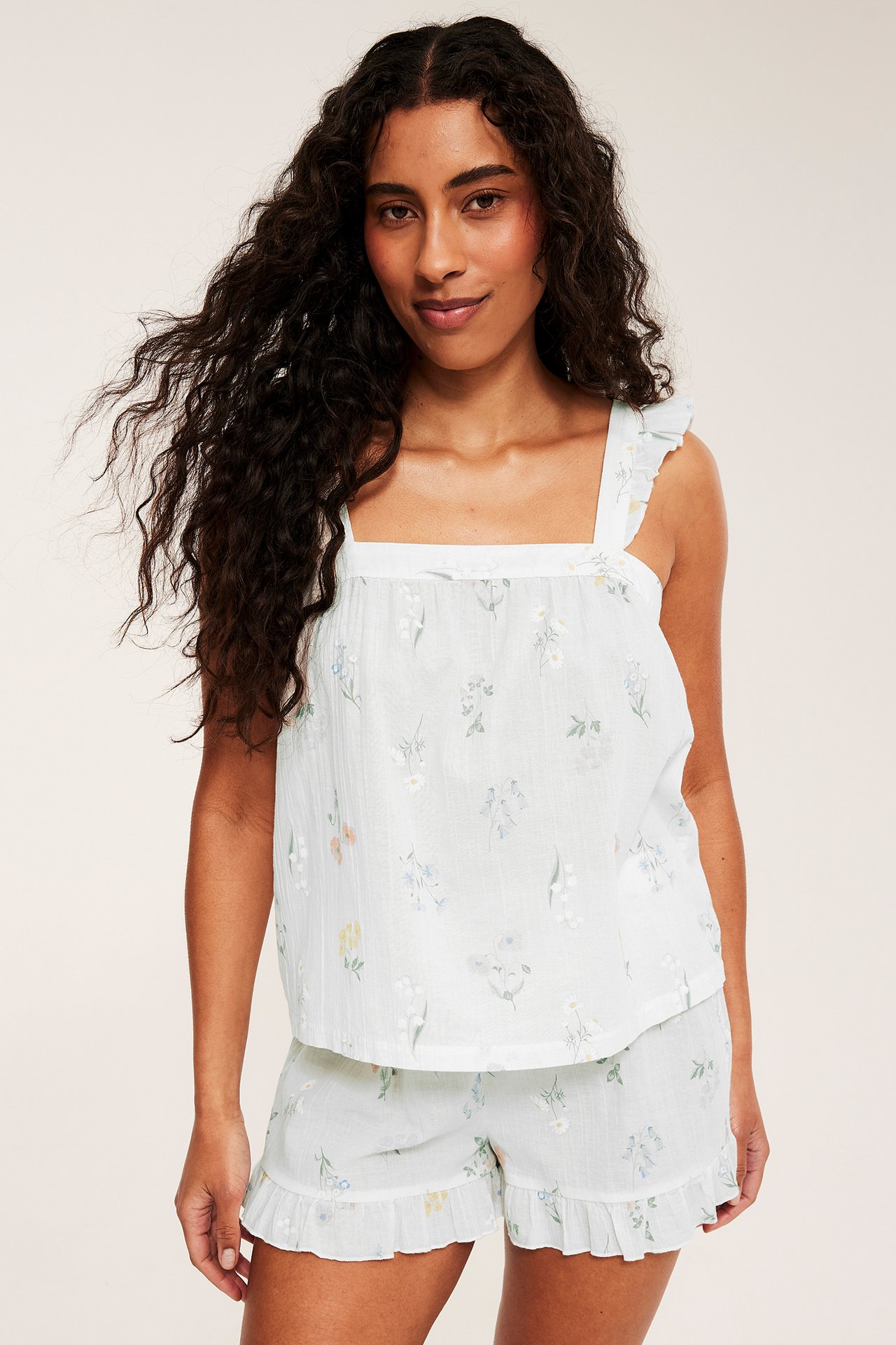 Edestäpäin: nainen luonnonvalkoisessa puuvillapyjamaksessa, kukkaprintti ja röyhelöt.