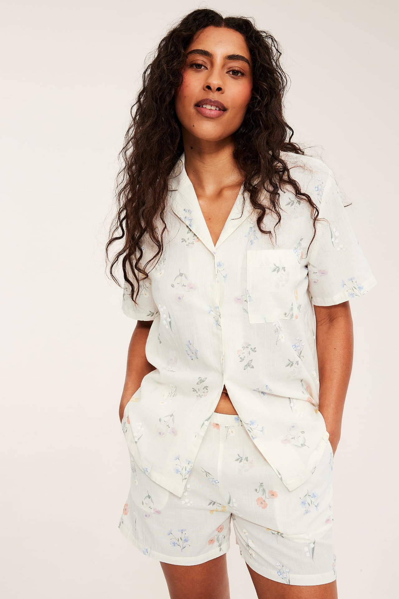 Widok z przodu: kobieta w kremowym bawełnianym zestawie piżamowym z kwiatowym wzorem, top i szorty.