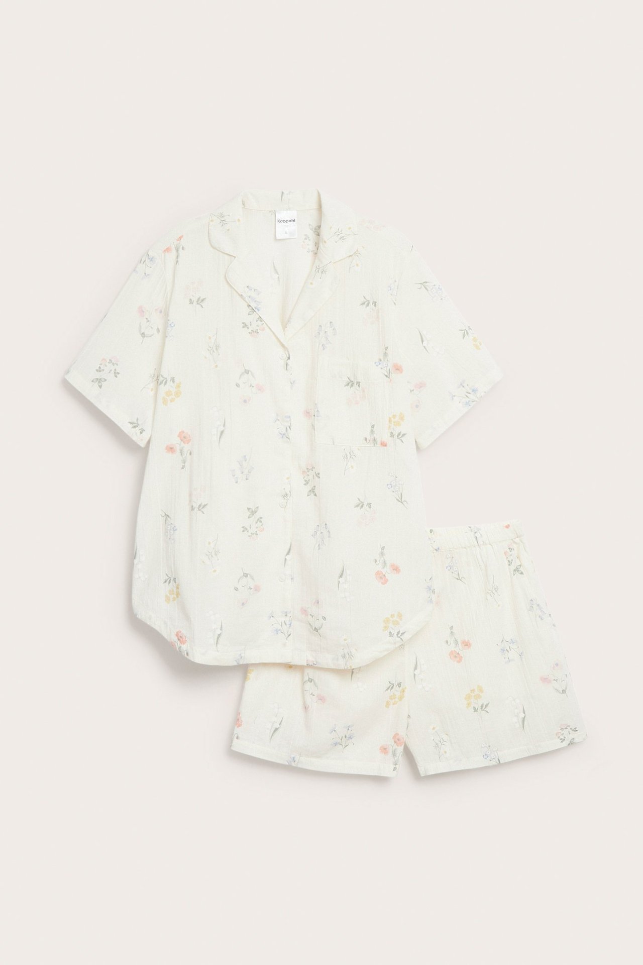 Frontbilde av et offwhite pyjamasett i bomull med kortermet blomstret skjorte og shorts.