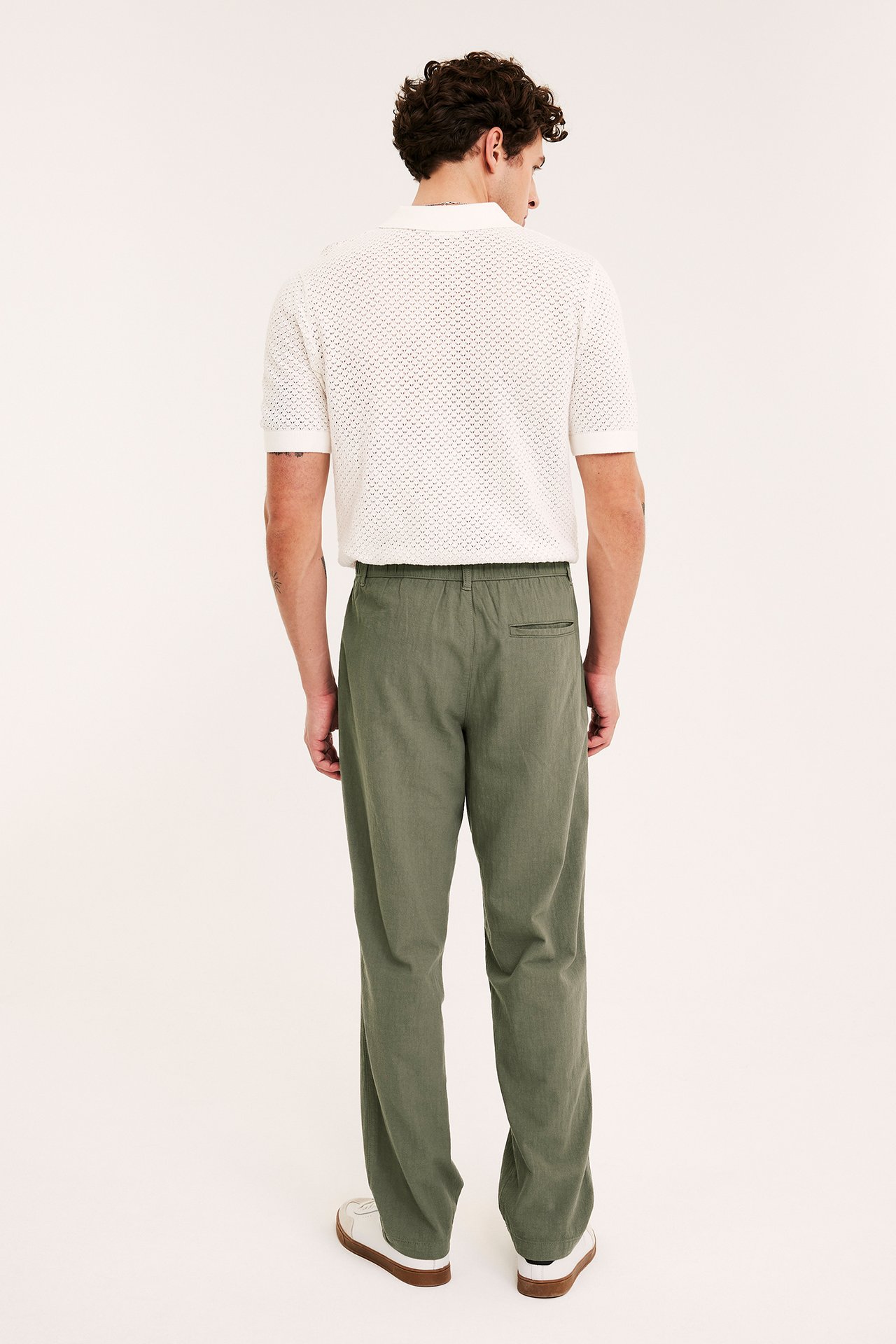 Mies takaa vihreissä puuvillahousuissa, joissa resori, ja luonnonvalkoisessa neulepoolopaidassa.