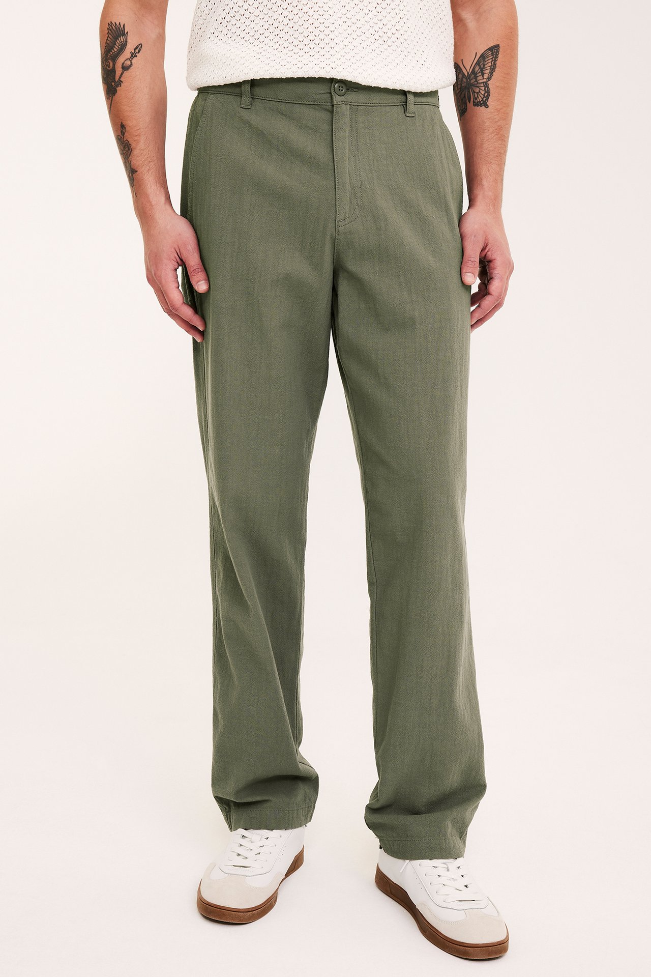 Forfra, mann i grønne regular fit bomullsbukser, en hvit strikket topp og hvite joggesko.