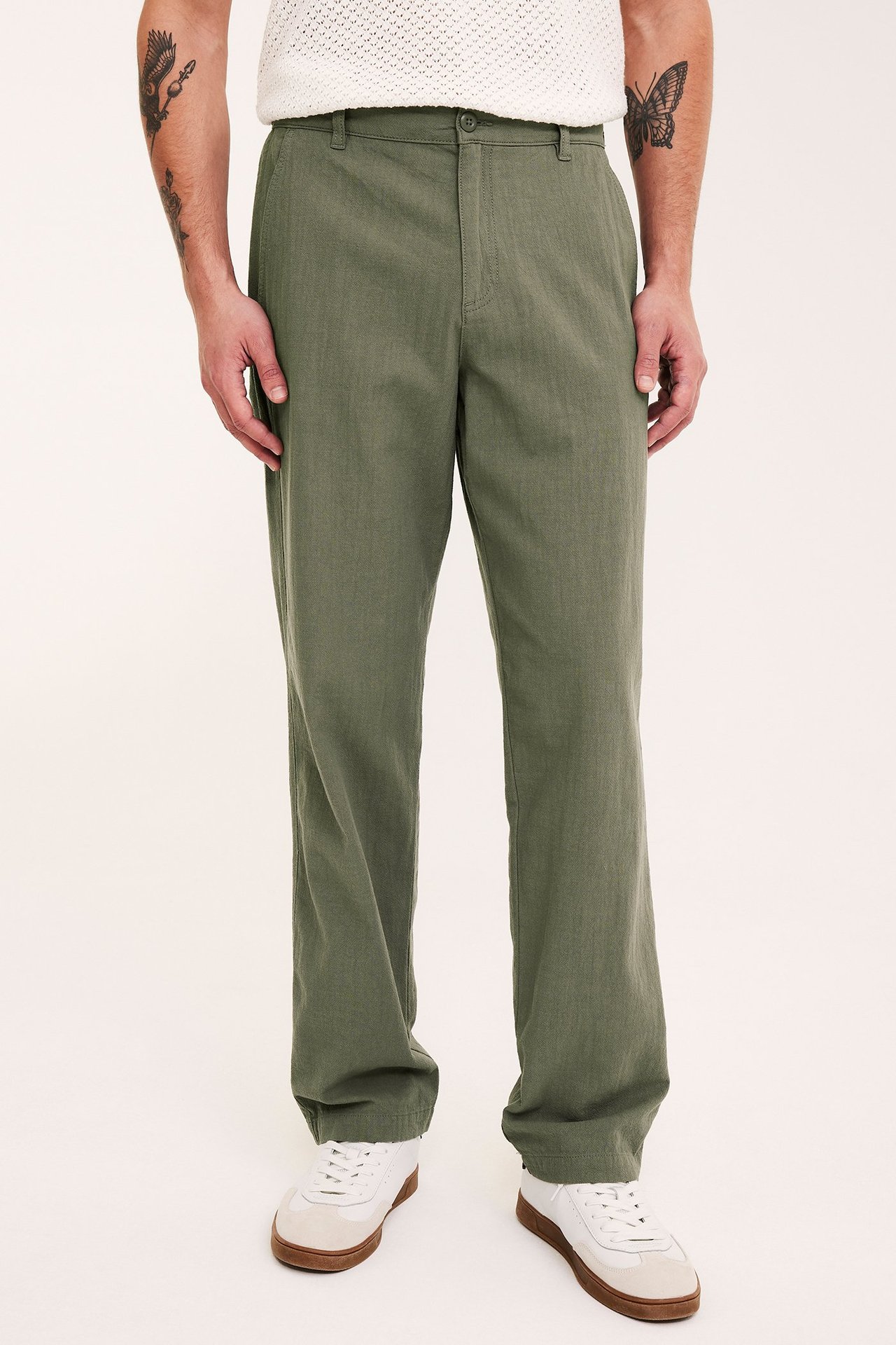 Framifrån, man i gröna regular fit bomullsbyxor, en vit stickad topp och vita sneakers.