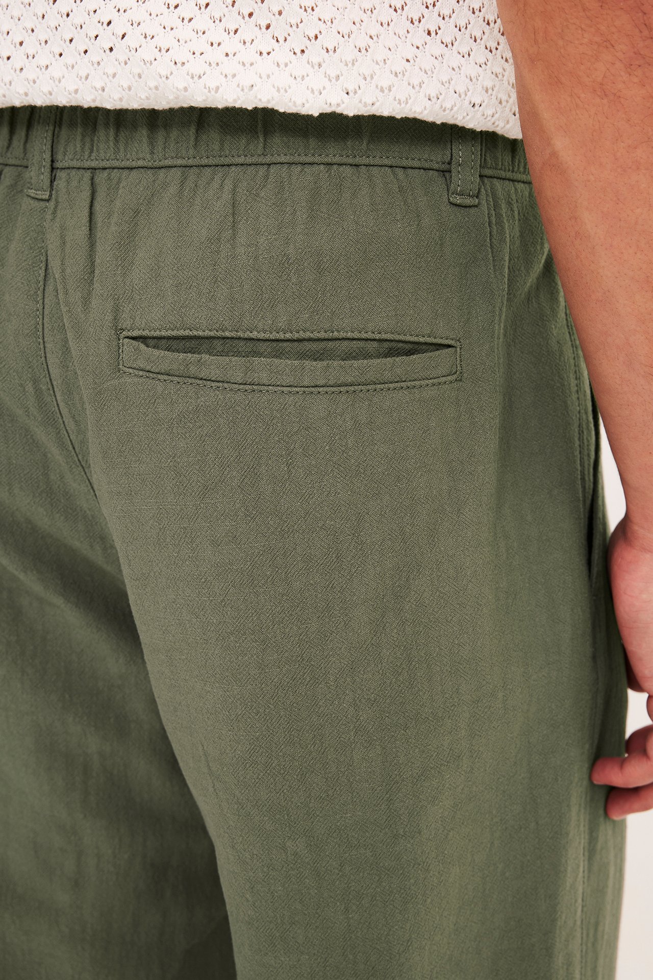 Lähikuva miehestä yllään vihreät puuvillahousut joustavalla vyötäröllä, takataskulla ja valkoinen neuletoppi.