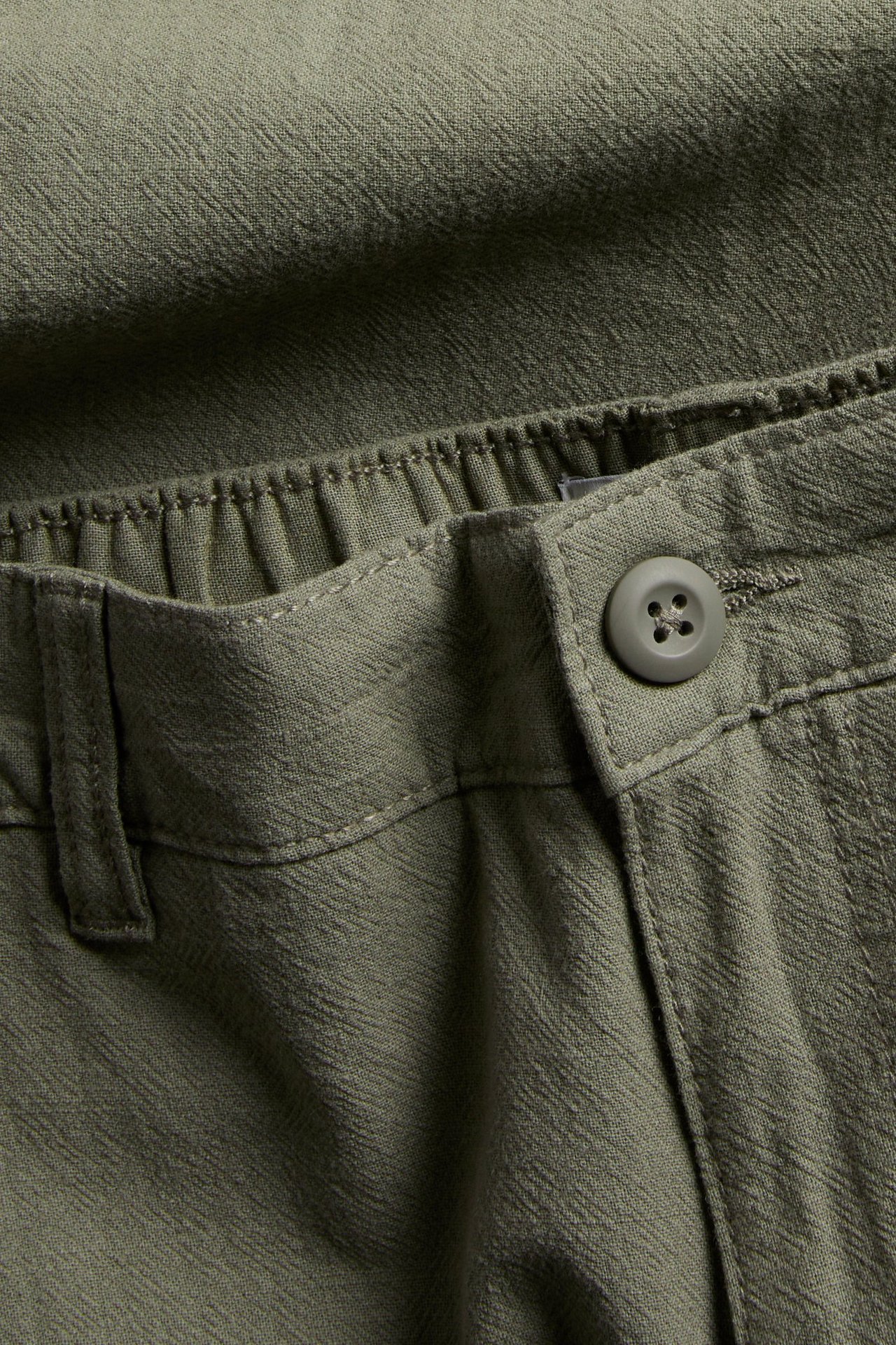 Zbliżenie zielonych bawełnianych spodni o regularnym kroju z lnem, zapinanych na guzik i z elastyczną talią.