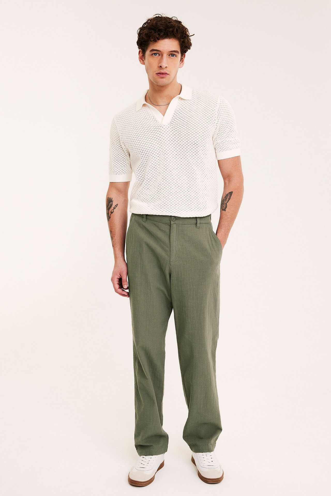 Mężczyzna z przodu w zielonych, bawełnianych spodniach regular fit, białej koszulce polo i białych sneakersach.