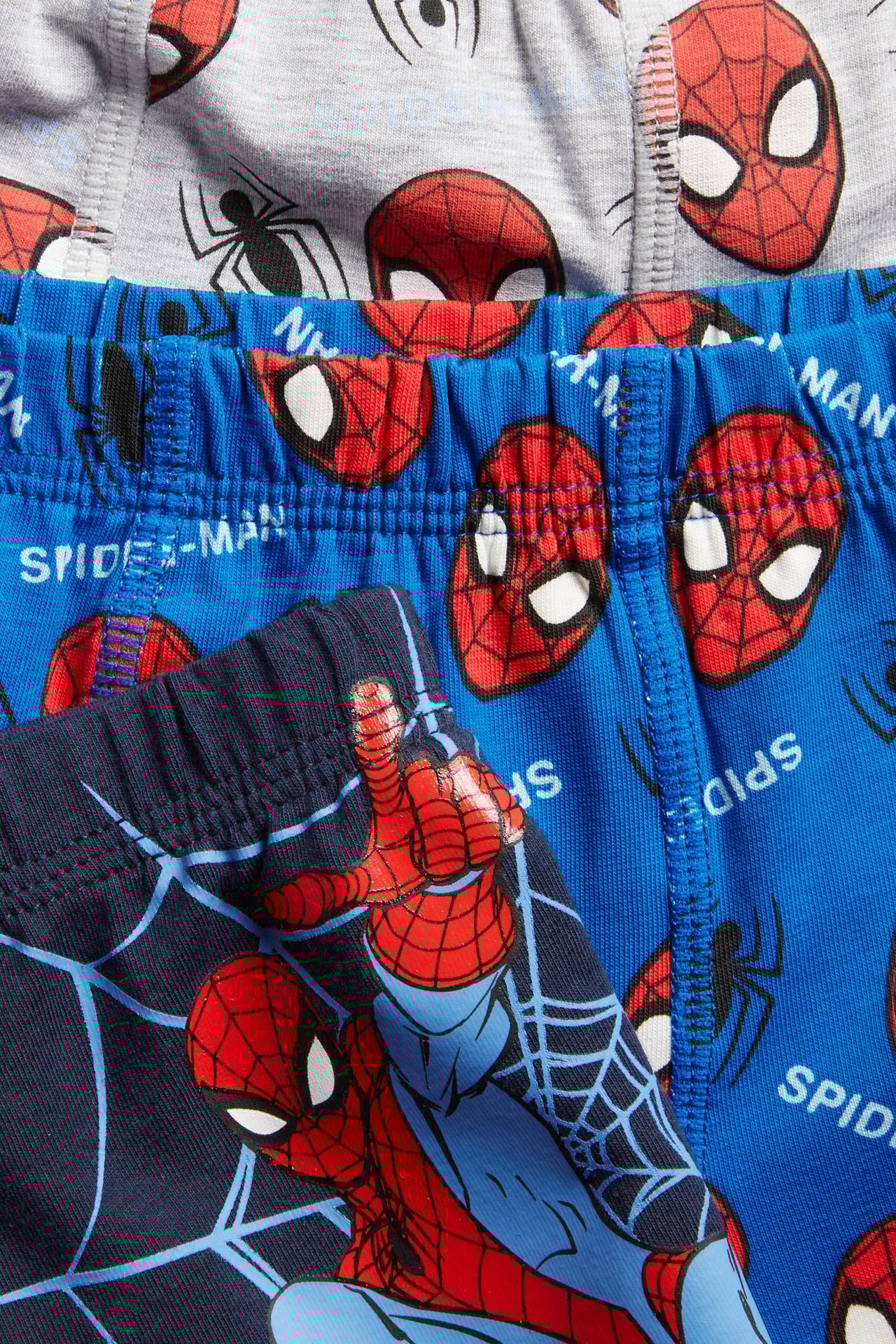 Zbliżenie na trzy bawełniane bokserki dziecięce: granatowe ze Spider-Manem, niebieskie z maskami i szare z maskami.