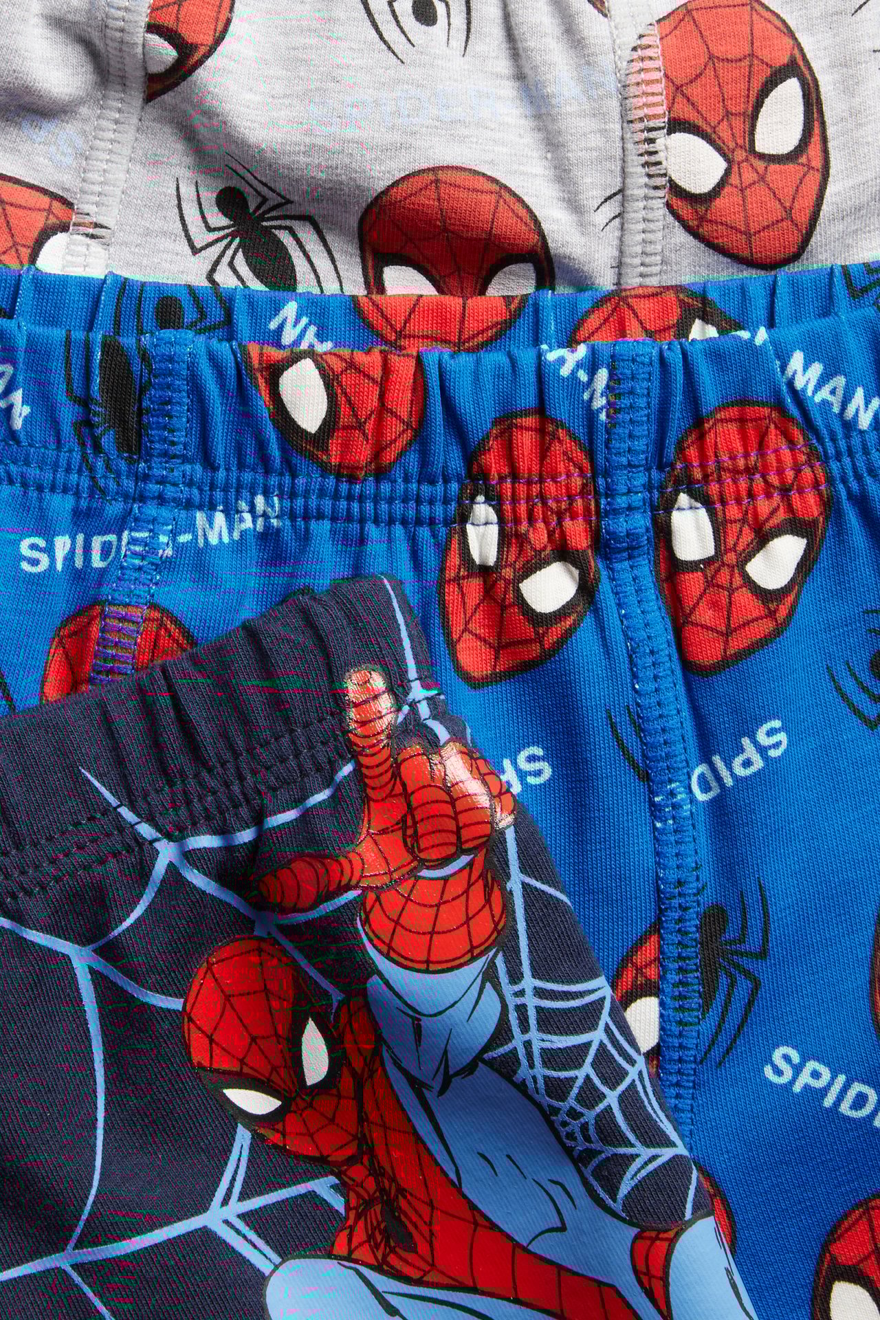 Närbild av mörkblå, kungsblå och grå boxerkalsonger med Spiderman-mönster för barn.
