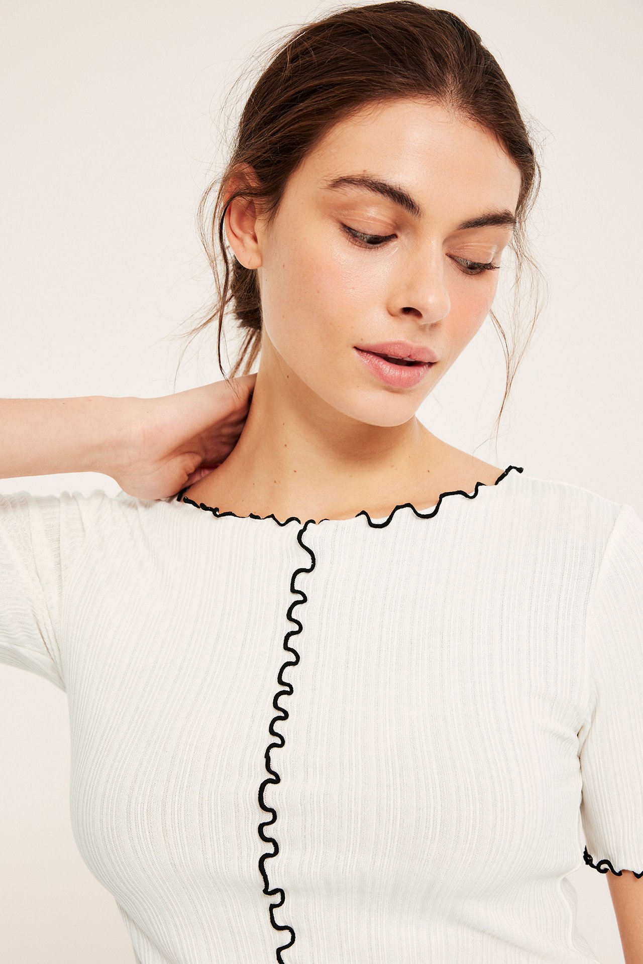 Närbild framifrån på en kvinna i en offwhite ribbad kortärmad topp med svarta babyoverlockkanter.