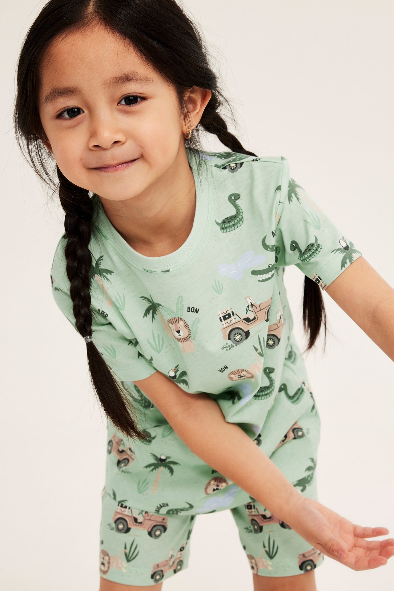 Nærbilde forfra av et barn i lysegrønn kortermet bomullspyjamas med heldekkende safari-trykk.