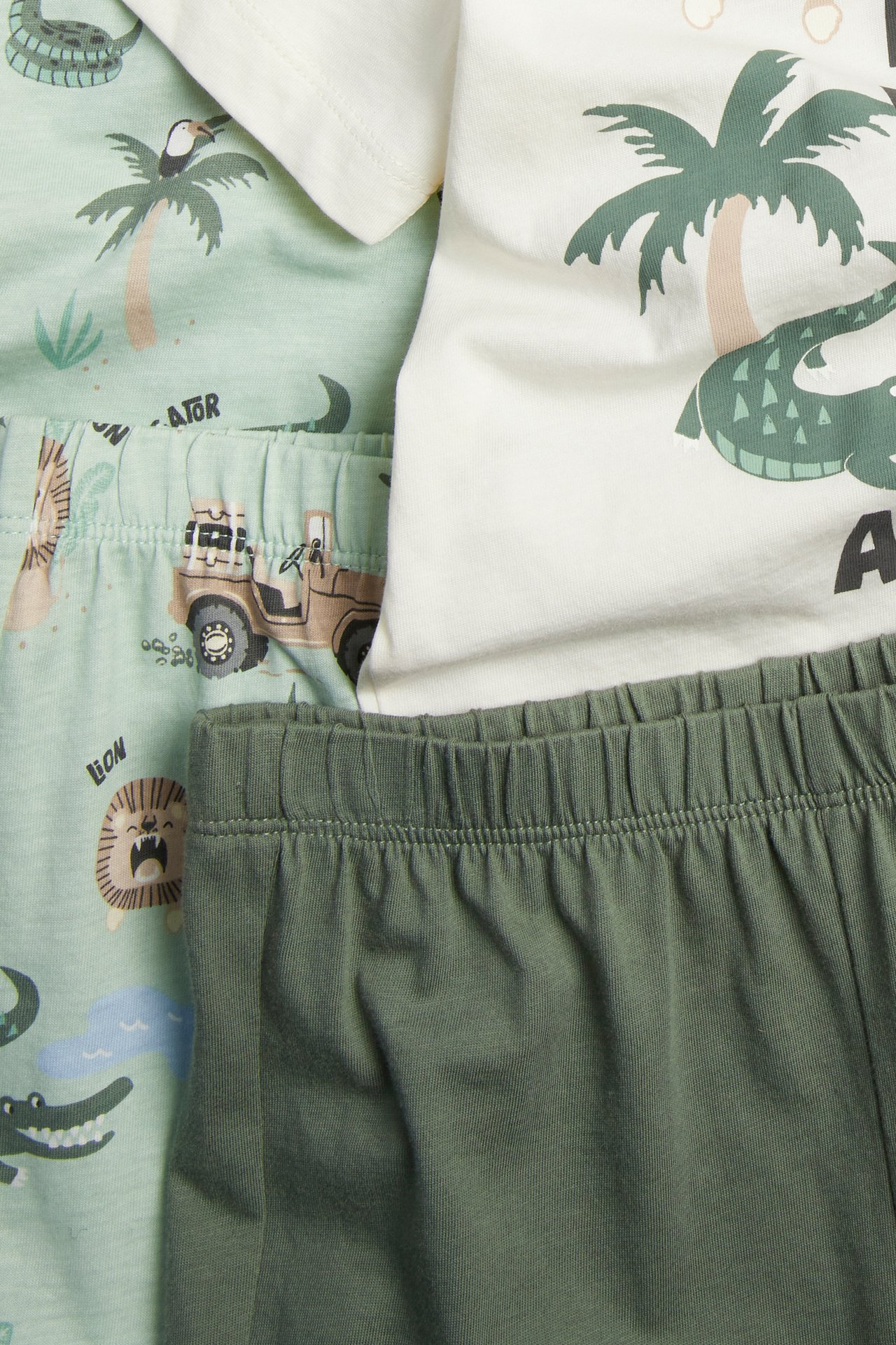 Zbliżenie: dwupak piżam dziecięcych; kremowy top z safari, oliwkowozielone spodnie i jasnozielone spodnie w całości we wzory.