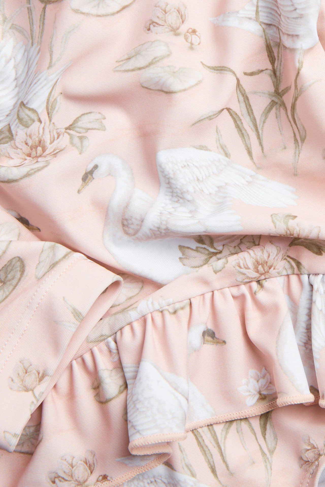 Zbliżenie różowego materiału stroju kąpielowego UV z białym wzorem łabędzi i kwiatów, z falbanką.