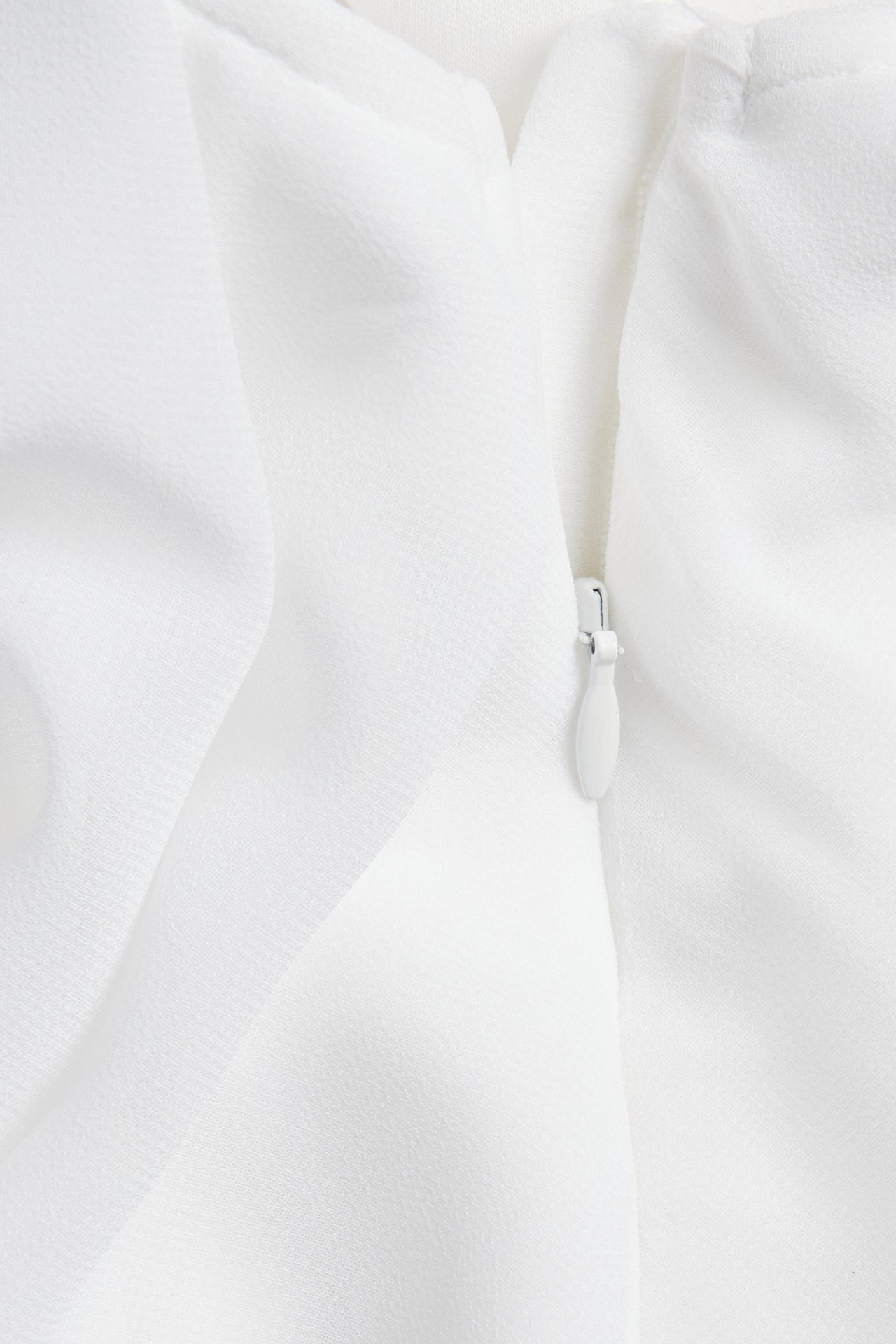 Zbliżenie białej bluzki z jednego ramienia z poliestru, ukazujące fakturę tkaniny i biały zamek.