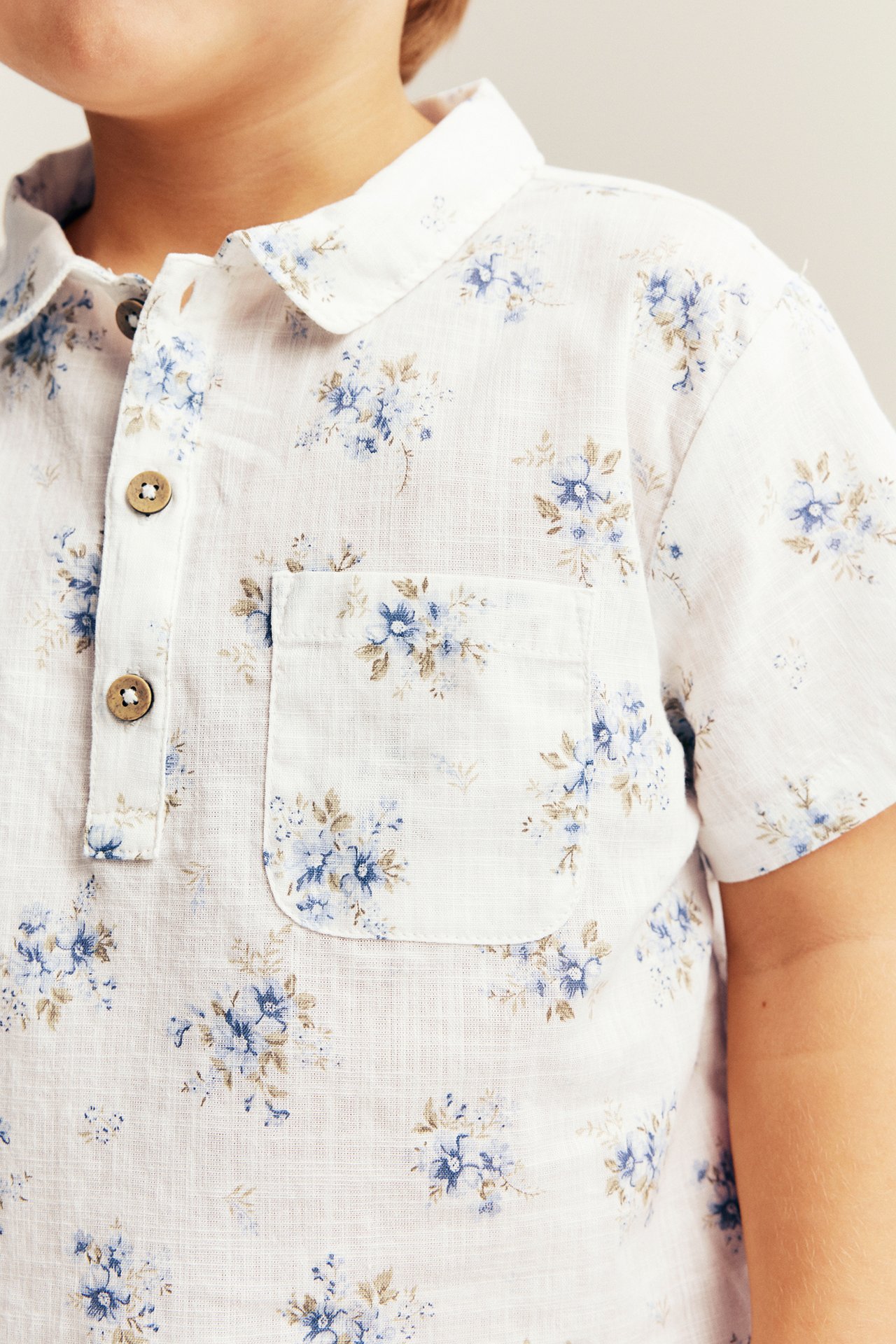 Nærbilde: Kids off-white kortermet bomullsskjorte med blått blomstermønster, krage og brystlomme.