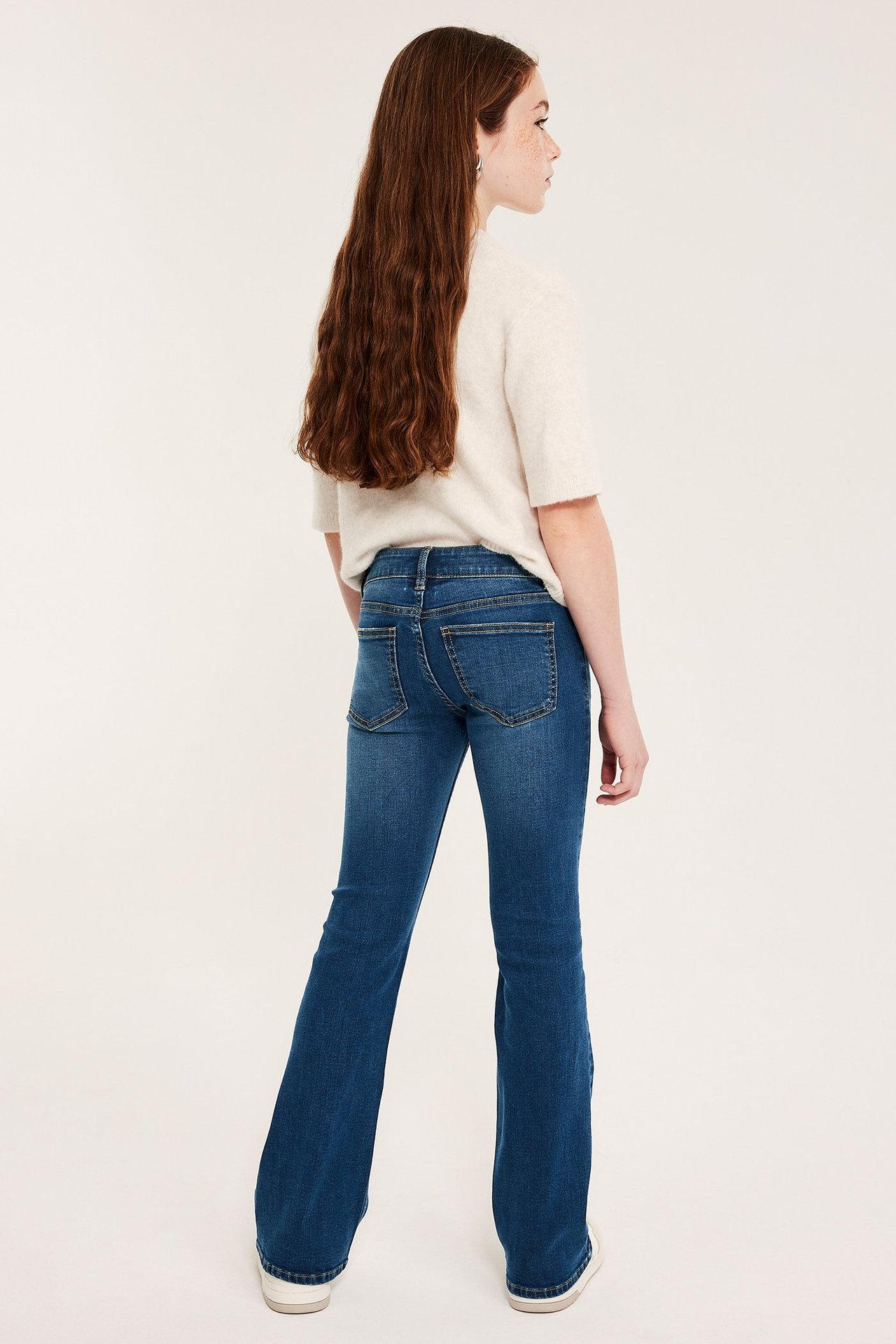 Bakfra: et barn i mørkeblå bootcut-jeans med lavt liv og en lys kortermet topp.