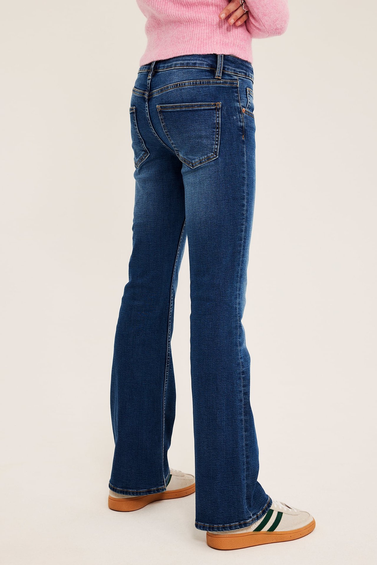 Bakfra: Mørkeblå utsvingte jeans for dame, en rosa strikket genser og offwhite joggesko.