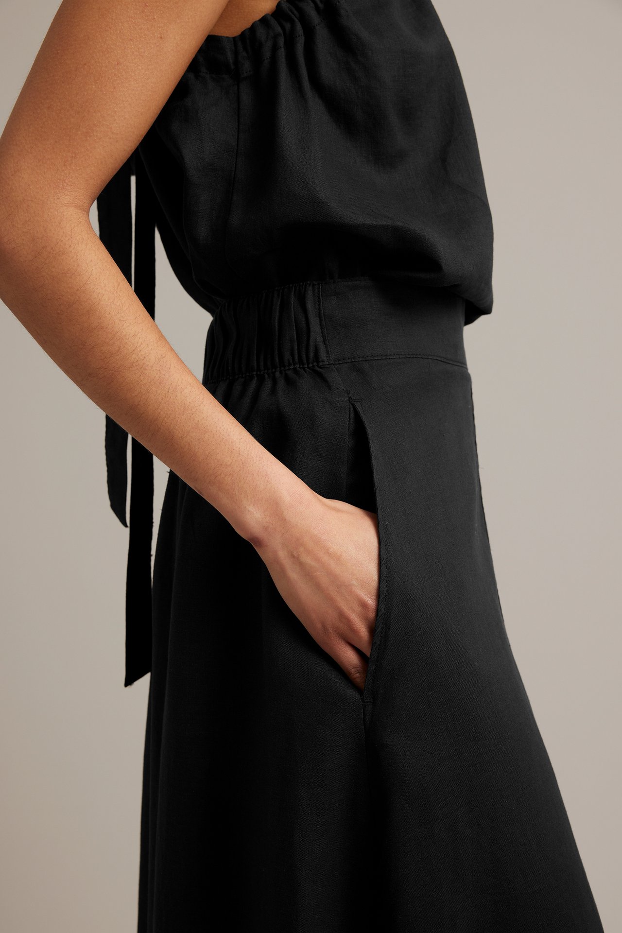 Sidovy av en kvinna i svart linnekjol med sidfickor och en matchande svart linnetopp.