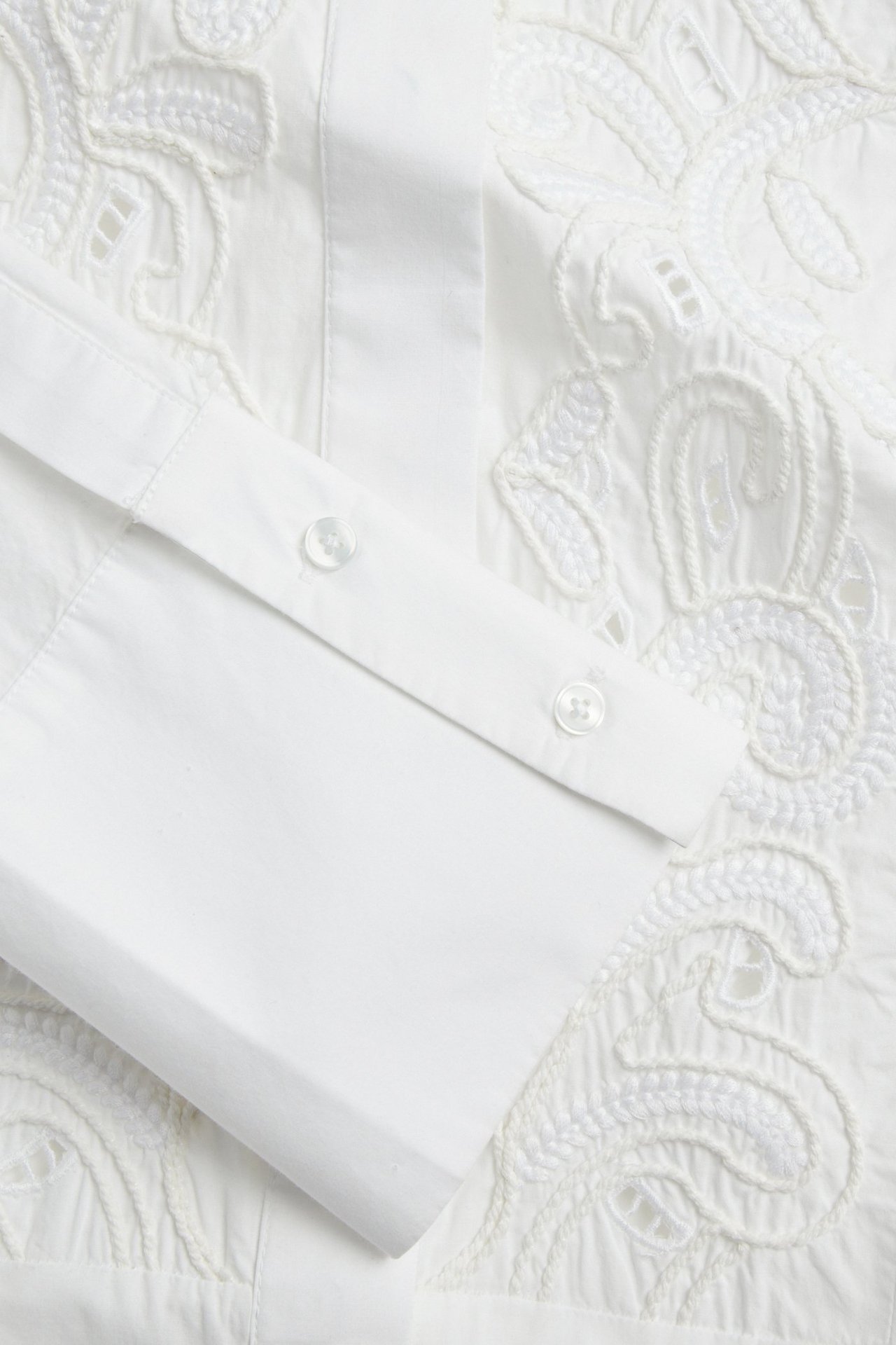 Zbliżenie na białą koszulę bawełnianą z białym haftem i mankietem zapinanym na dwa guziki.