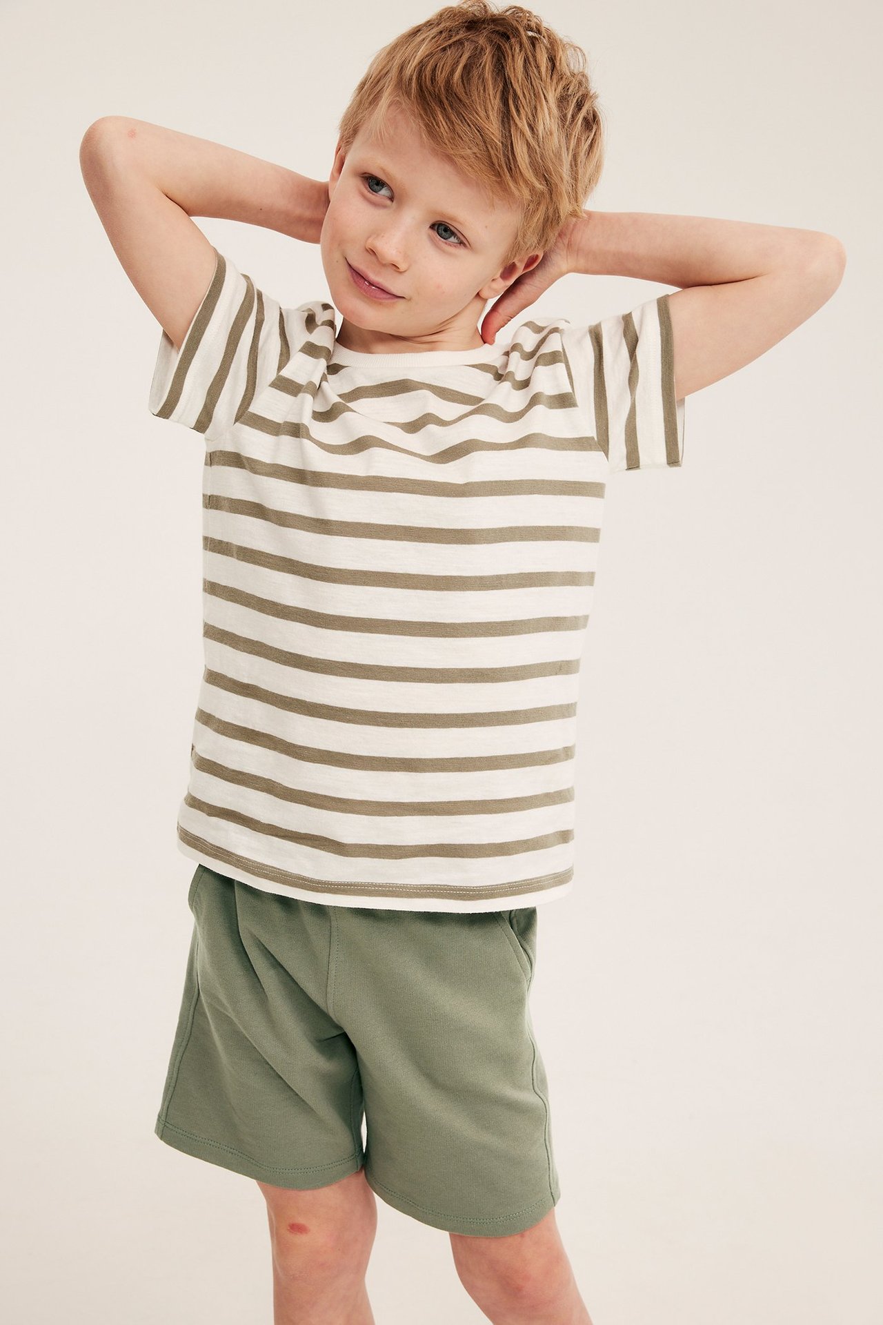 Frontvy av ett barn i mörkgröna bomullsjersey-shorts och en randig vit och beige t-shirt.