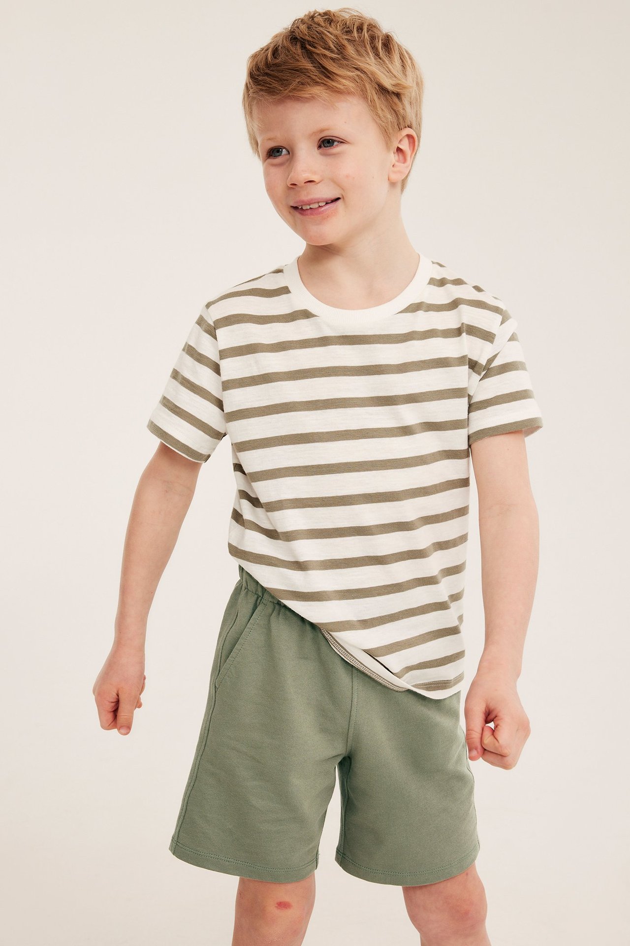 Widok z przodu: Dziecko w ciemnozielonych bawełnianych szortach jersey i biało-oliwkowej koszulce w paski.