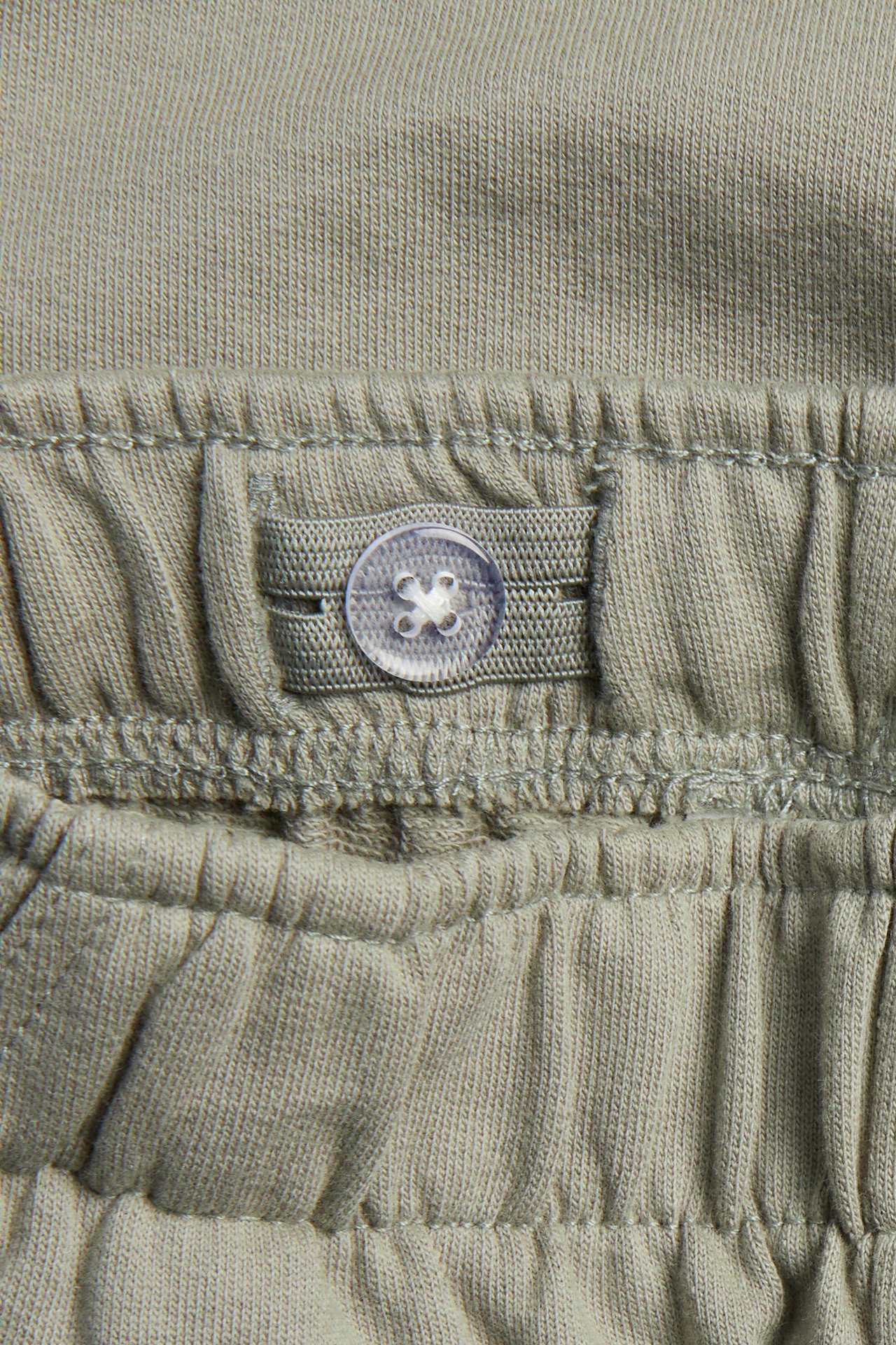 Närbild av mörkgröna mjukisshorts i bomull med justerbar knapp i midjan.