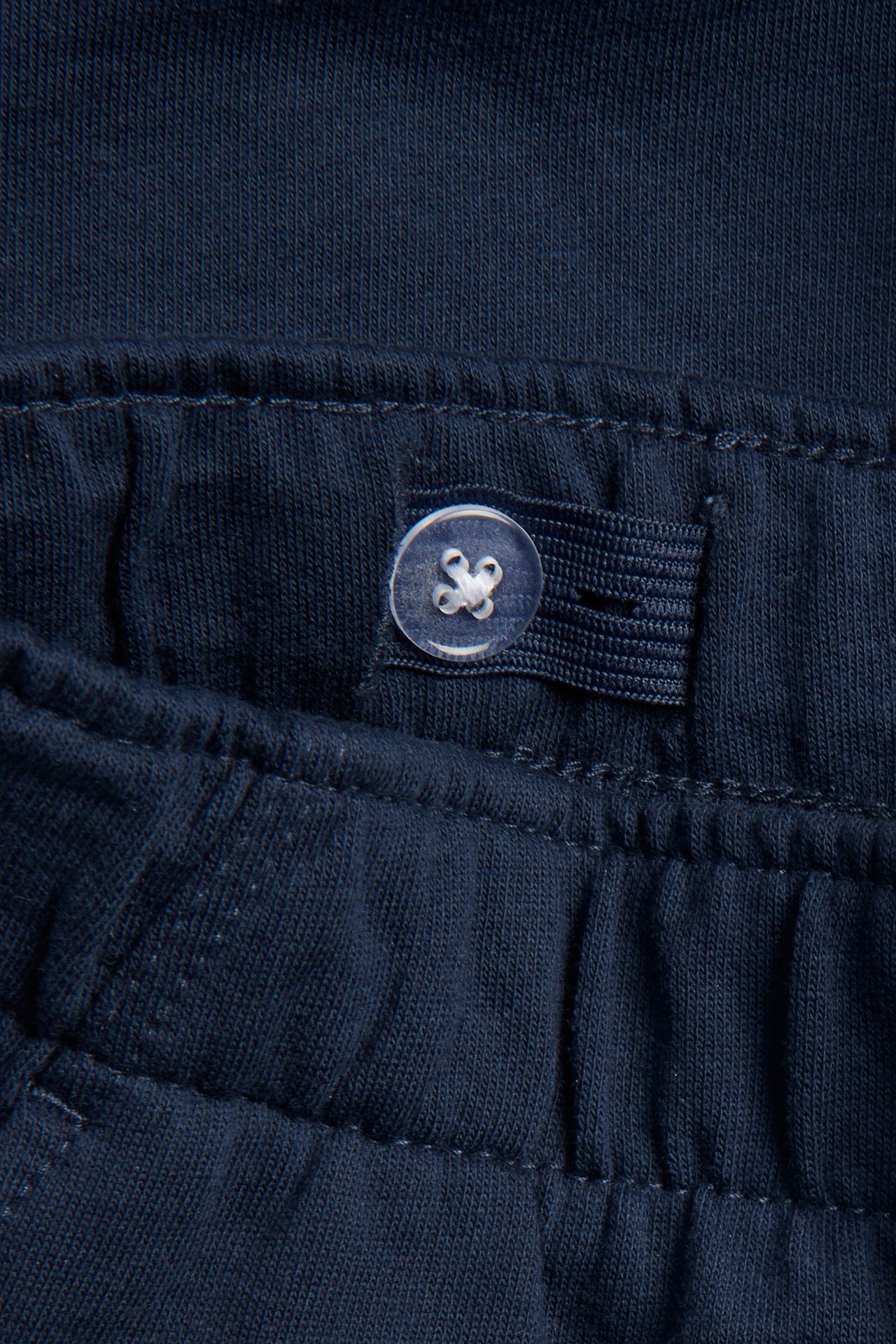 Närbild av mörkblå bomulls-mjukisshorts med justerbar knapp och resår i midjan.