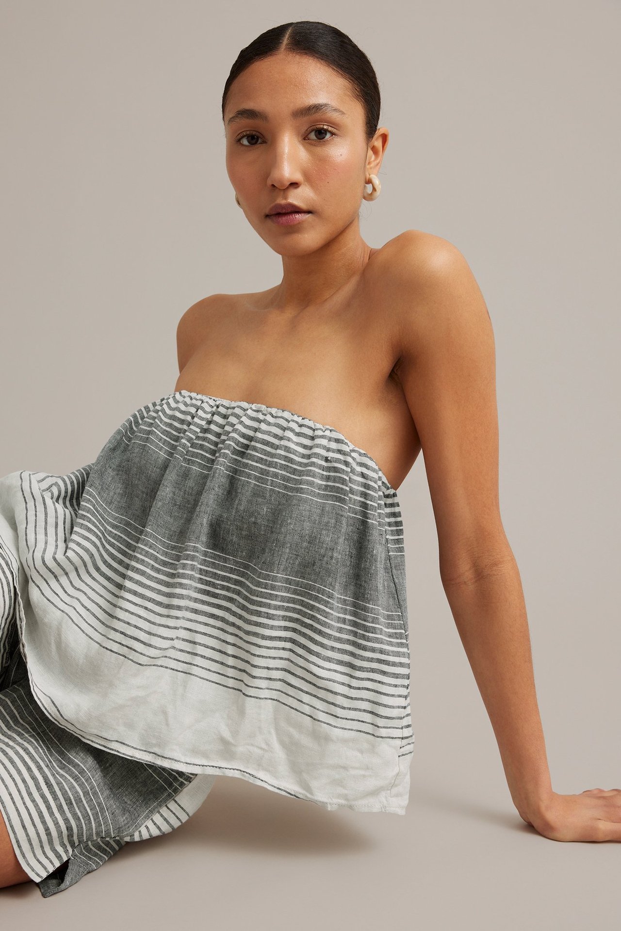Frontvisning: Kvinne i mørkegrå og hvitstripet stroppeløs lintopp med elastisk kant.