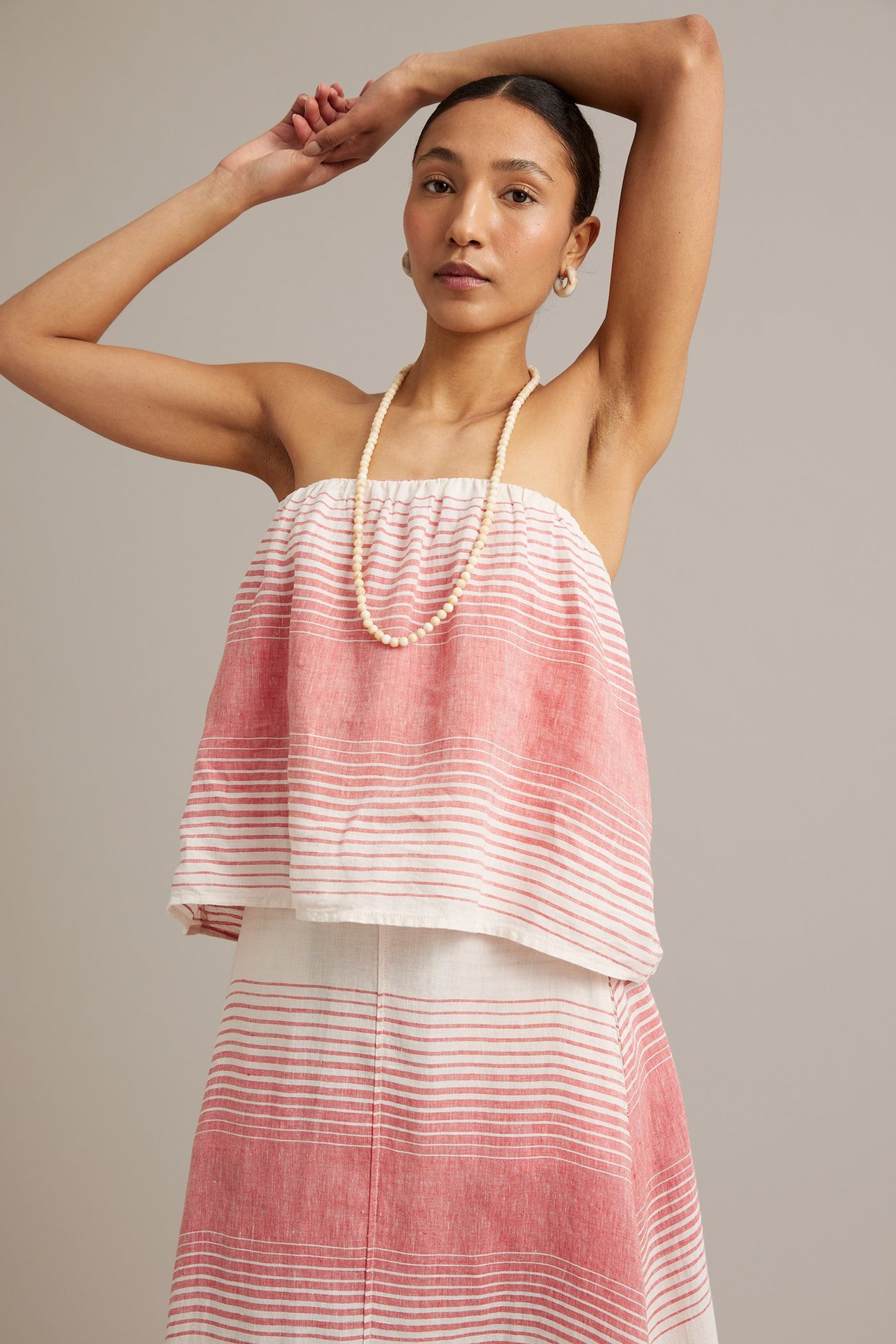 Frontvy: Kvinna i randig röd och vit linnebandeau-topp, matchande kjol och pärlhalsband.