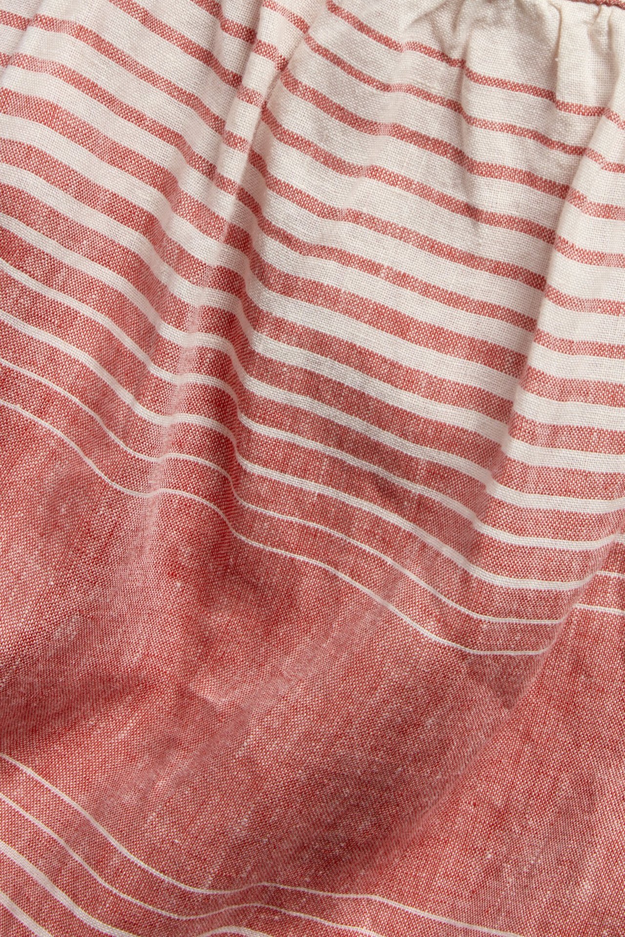 Närbild av ett rött och vitt randigt linne i linne med veckad överkant.