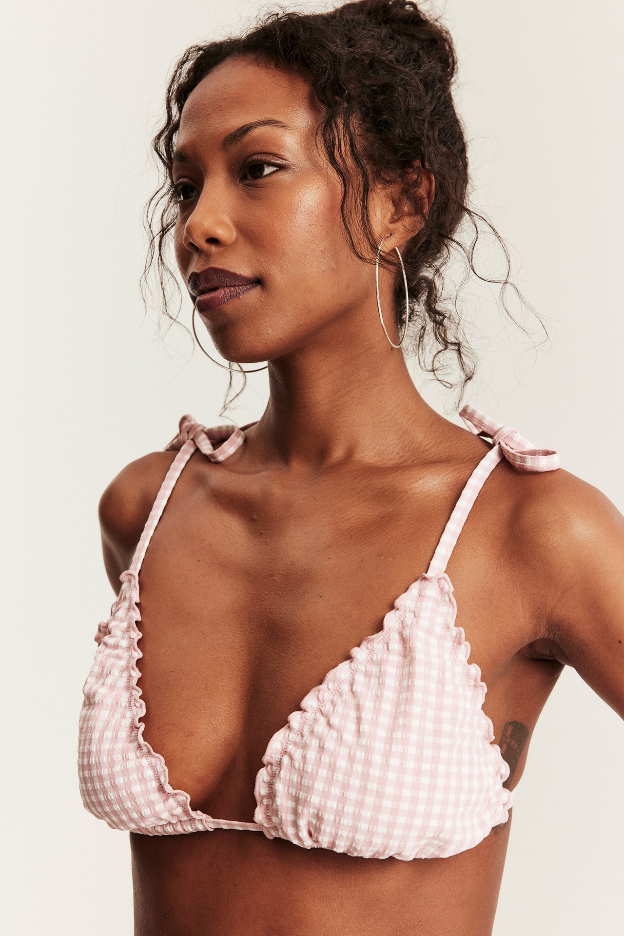 Widok z przodu: kobieta w różowo-białym bikini topie w kratkę, wiązane ramiączka, srebrne kolczyki.