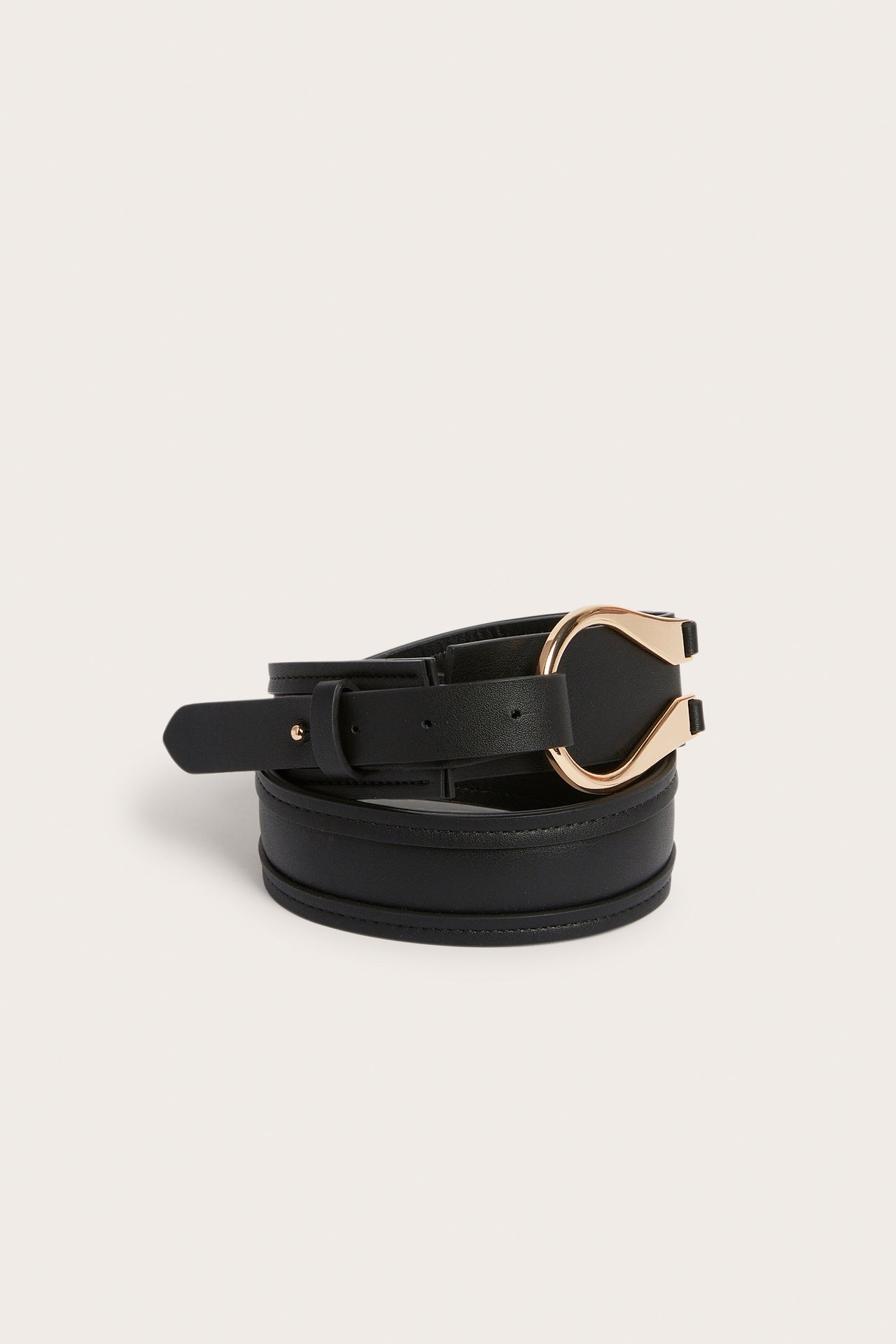 Nærbilde av et svart belte i skinnimitasjon med en dekorativ gullfarget metallspenne, brettet og festet.