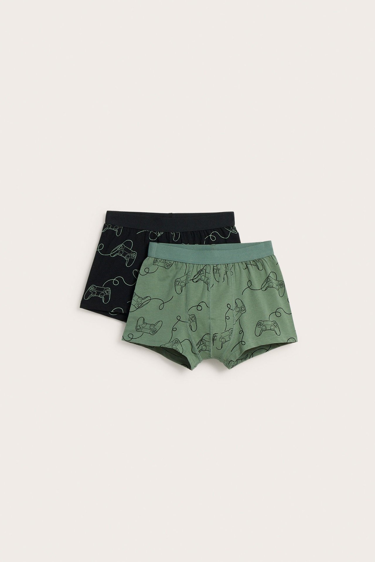 Front view av två par barnboxerkalsonger: en grön, en svart, båda med gaming-kontrollmönster.