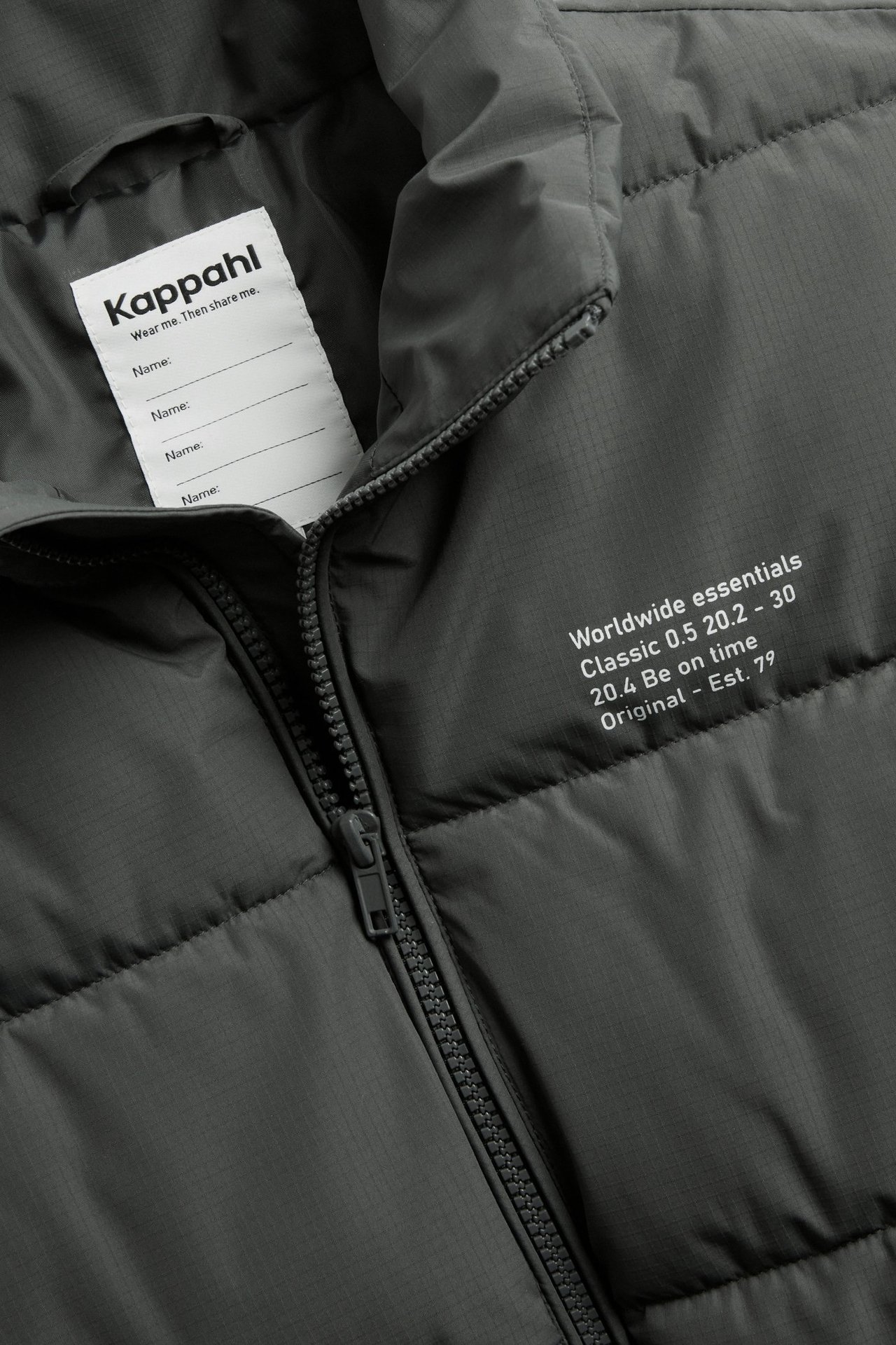 Zbliżenie czarnej, strukturalnej kamizelki puchowej z zamkiem błyskawicznym i białą metką Kappahl.