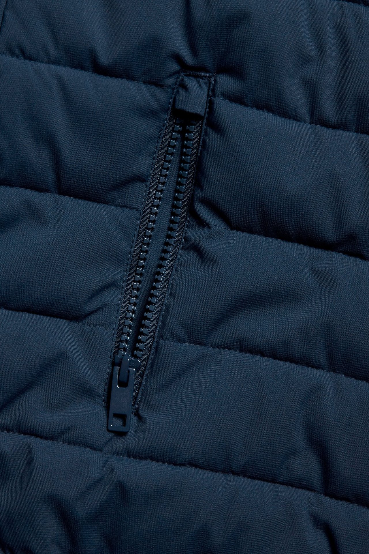 Zbliżenie ciemnoniebieskiej pikowanej lekkiej kurtki z kieszenią na zamek.