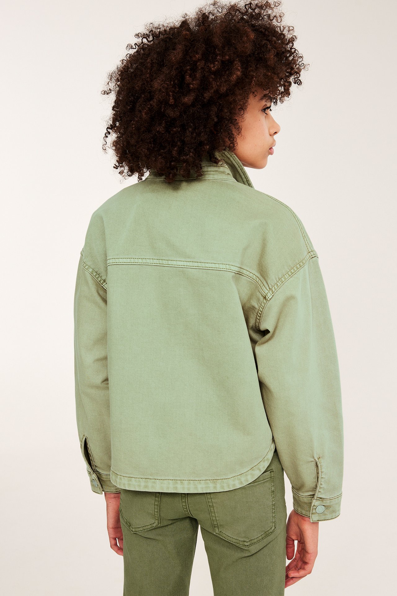 Ryggvy av ett barn i en grön tvättad bomullstwilljacka och matchande gröna byxor.