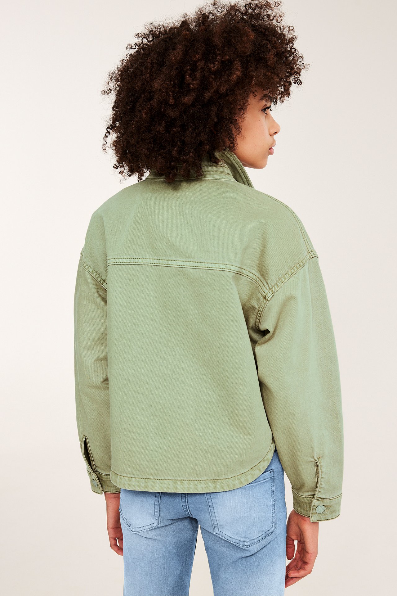 Ryggvy på ett barn i grön tvättad bomullstwilljacka och ljusblå jeans.