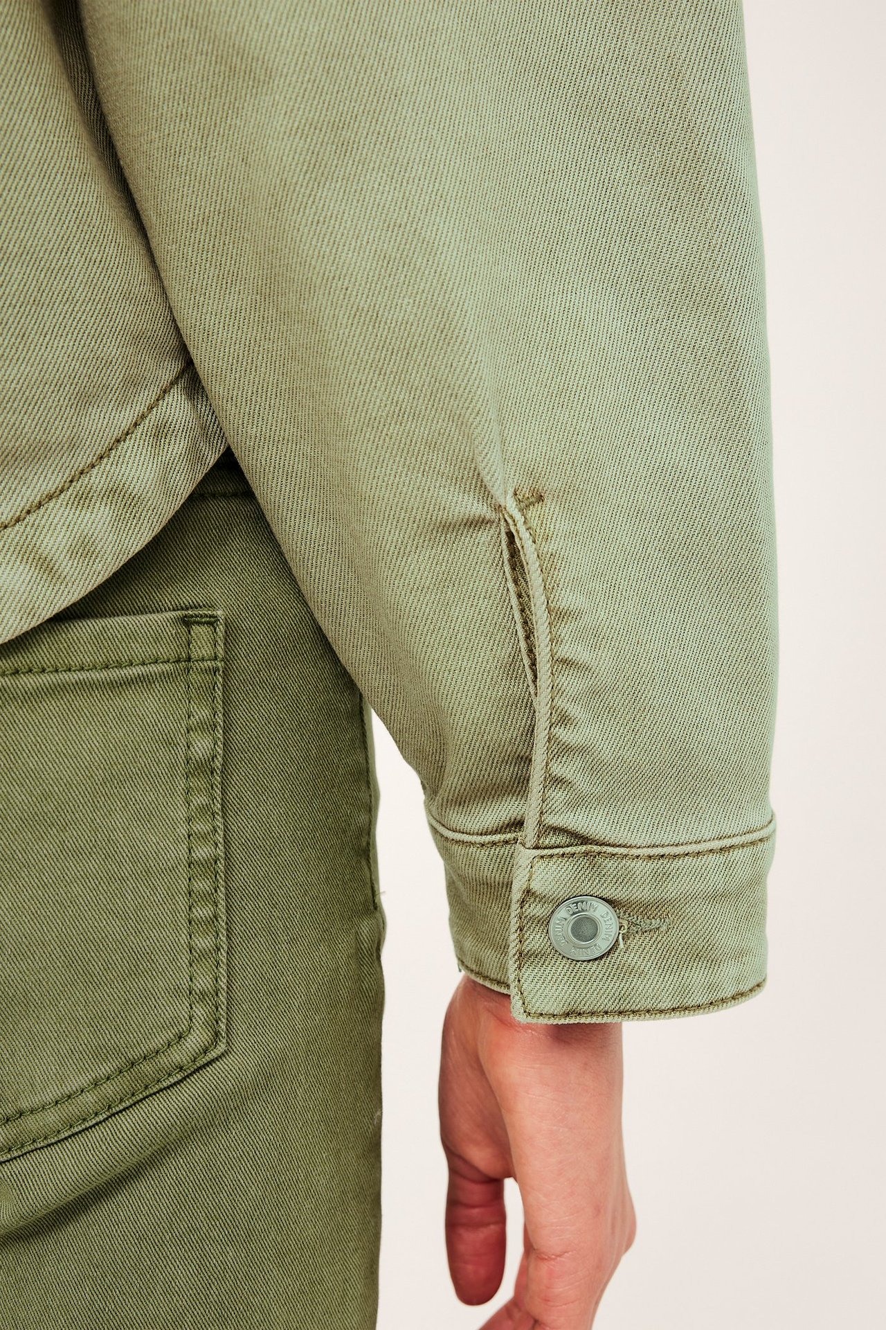 Närbild på en grön jackärm i tvättad bomullstwill med knappmanschett, matchande gröna byxor syns.