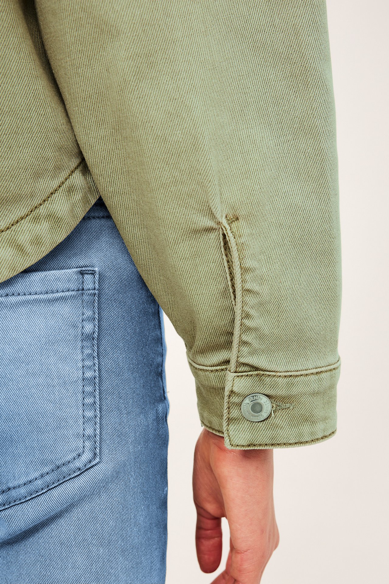 Närbild av kvinnas gröna tvättade bomullstwilljackärm med knappmanschett, över blå jeans.