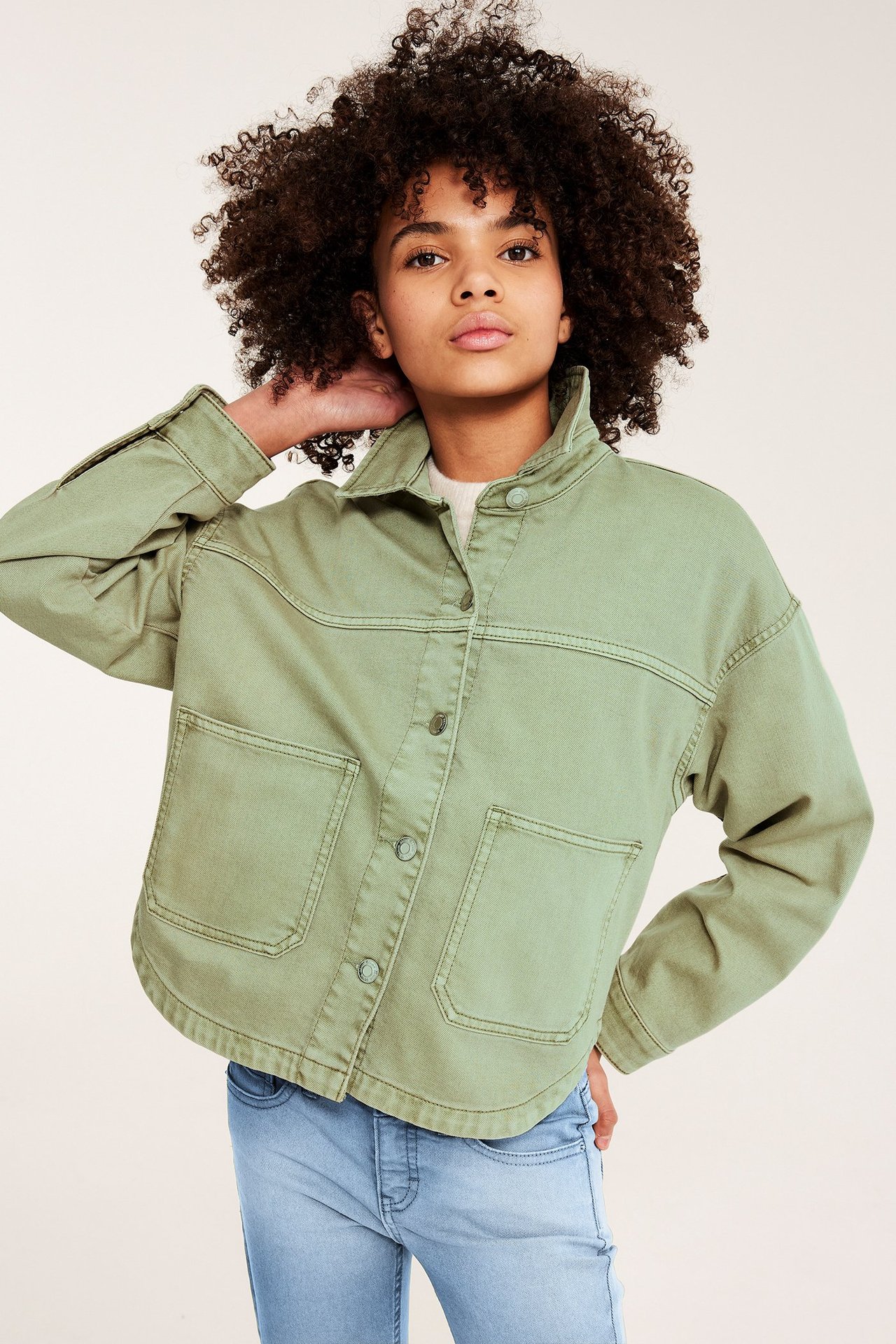 Forfra: Et barn har på seg en grønn jakke i vasket bomullstwill med knapper og lommer.