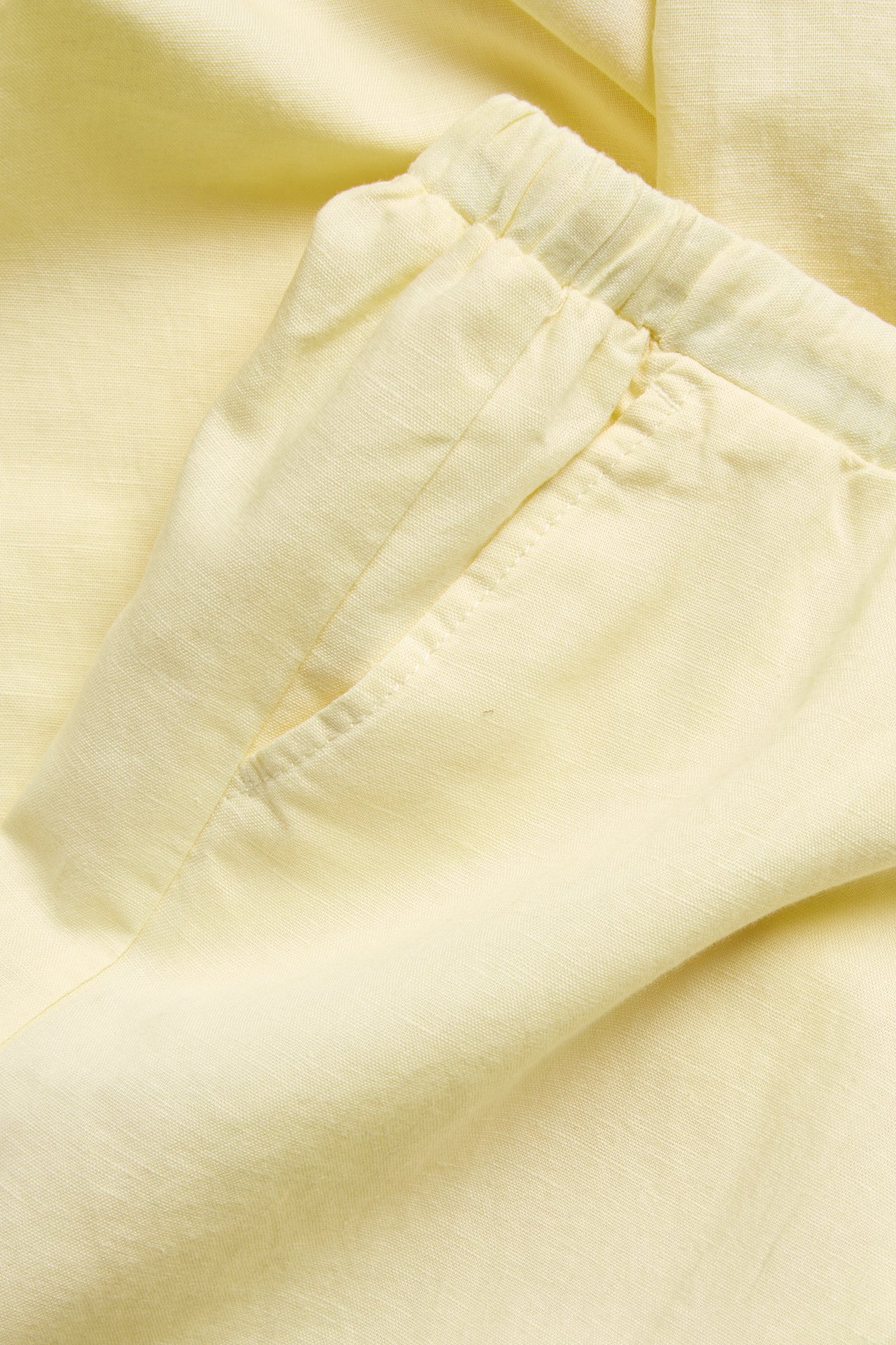 Nærbilde av lys gul linblanding bukse med elastisk snøring i midjen og en frontlomme.