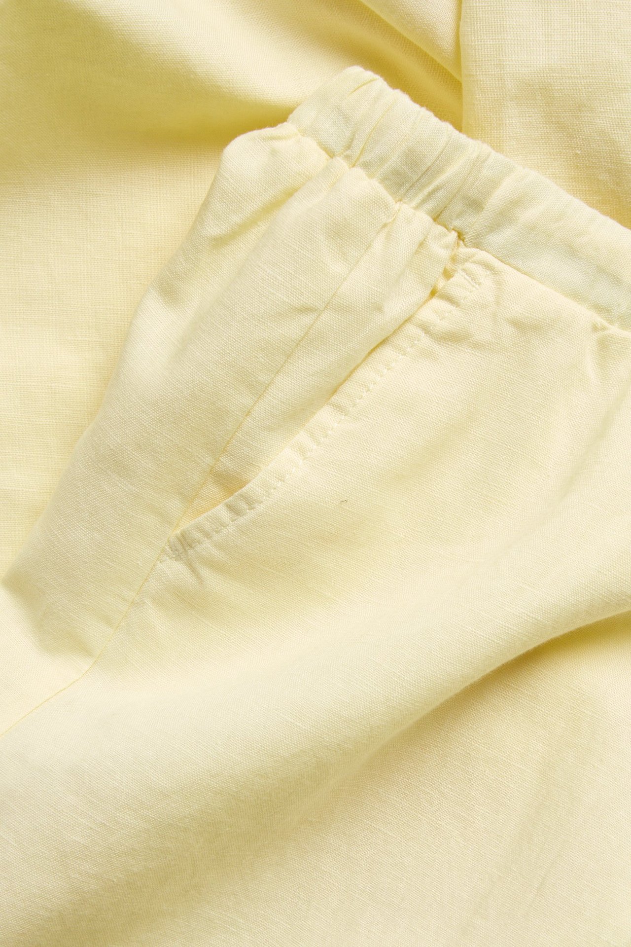 Lähikuva vaaleankeltaisista pellavasekoitehousuista, joustava kiristysnyörivyötärö ja etutasku.