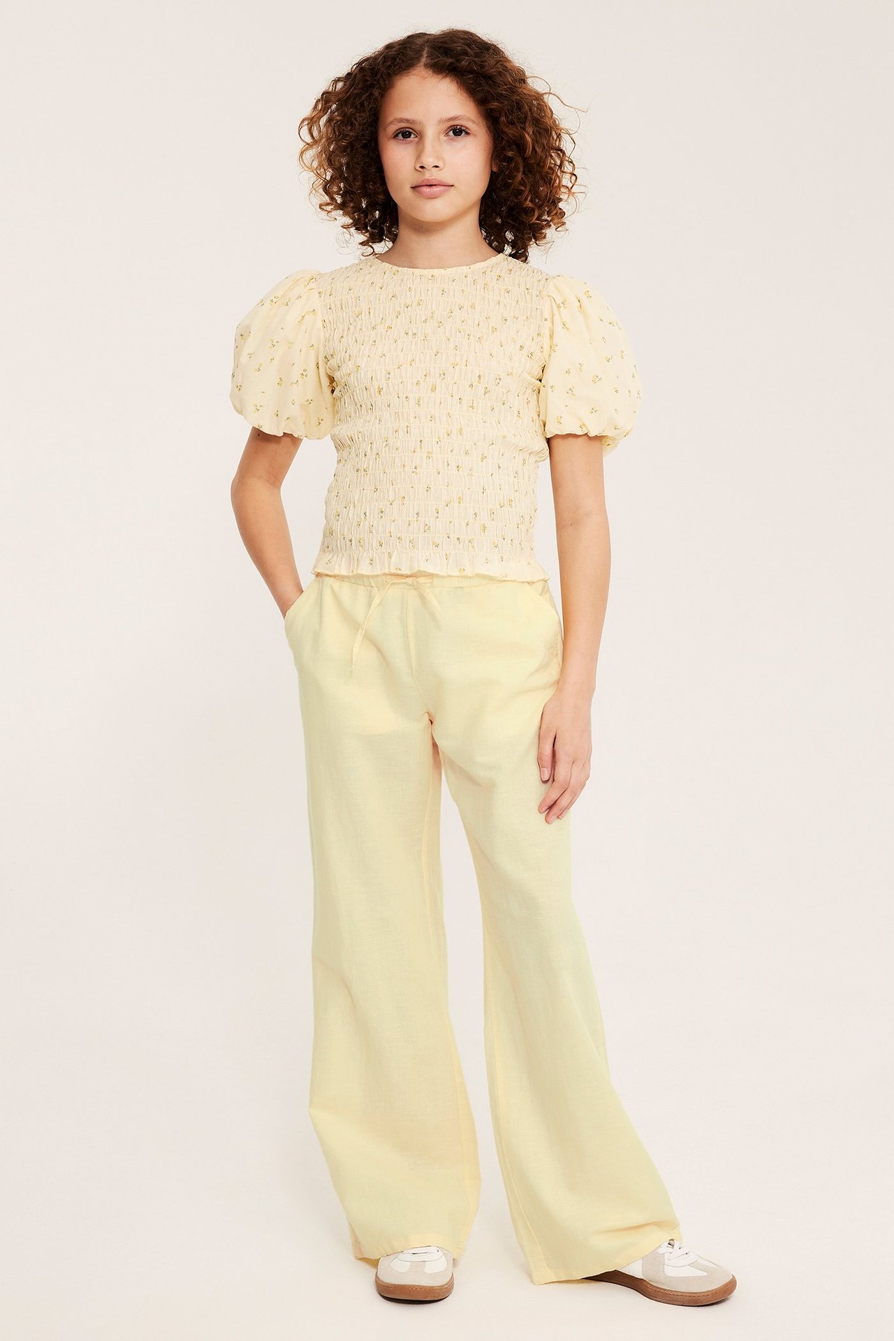 Widok z przodu: Dziecko w jasnożółtych spodniach lnianych z elastyczną talią i marszczonym żółtym topie.