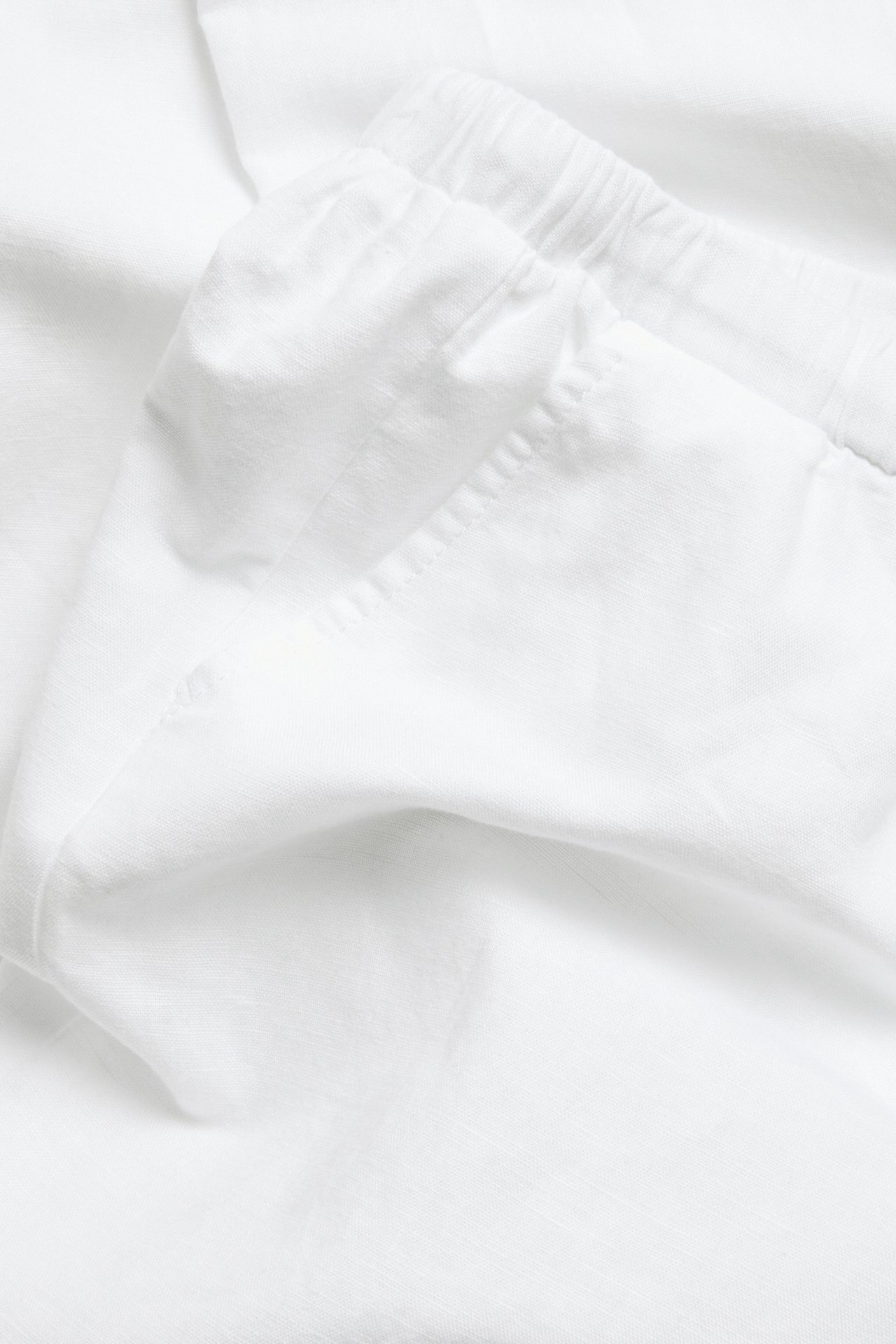 Nærbilde av hvite linblandingsbukser som viser den elastiske linningen og stoffets tekstur.