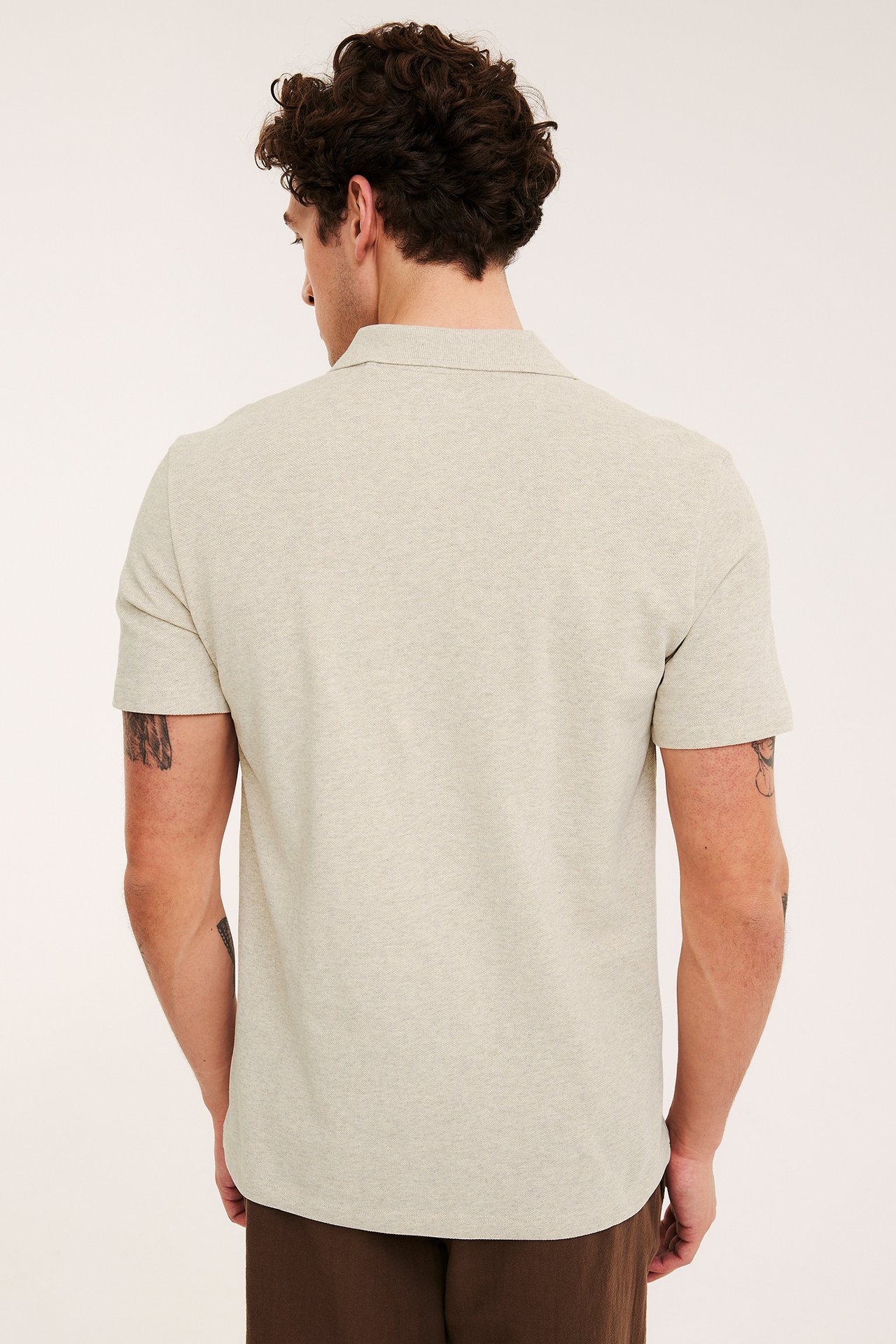 Bakfra av en mann iført en beige melert piképoloskjorte i bomullspiké med brun bukse.