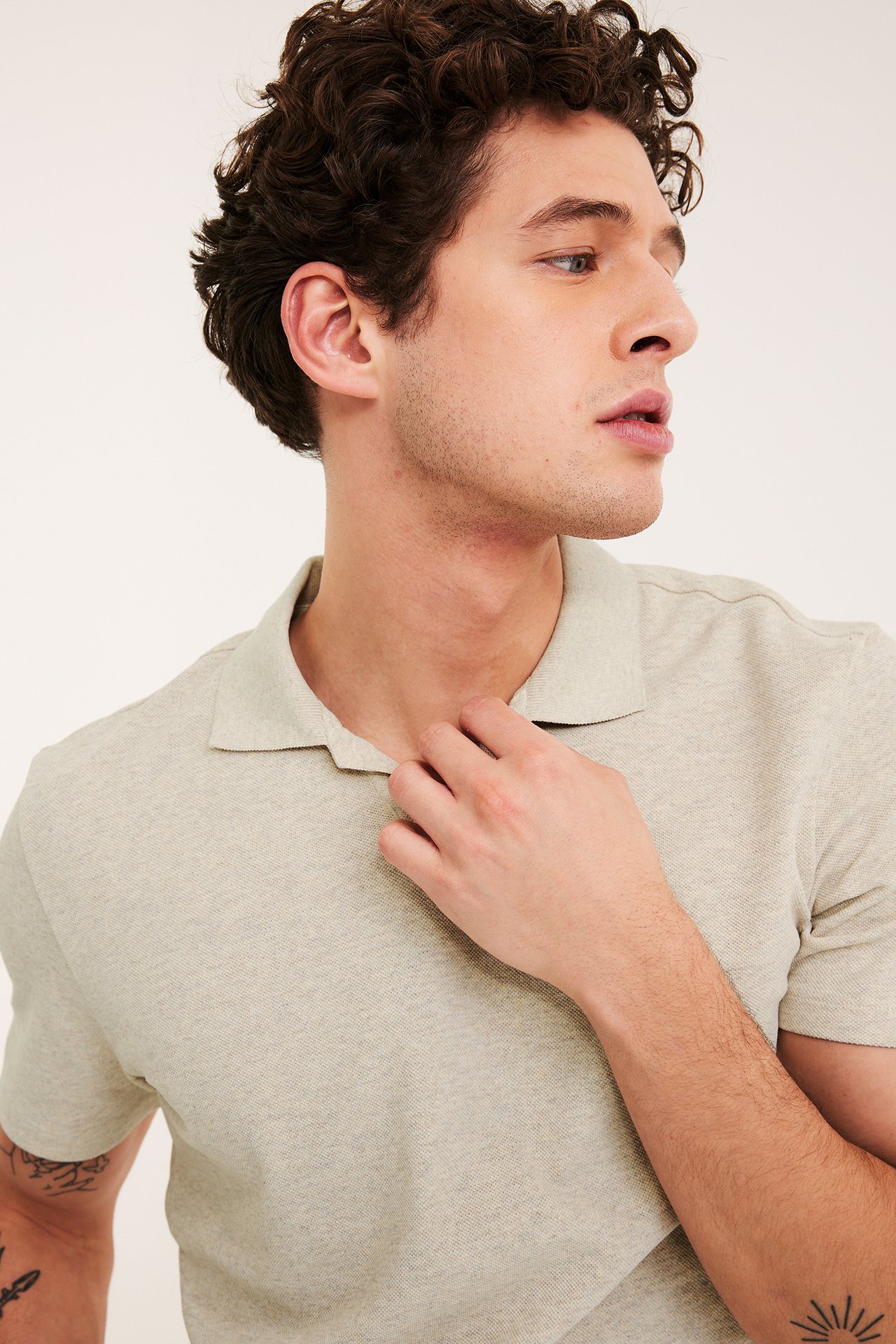 Nærbilde, sideblikk av en mann i melert beige piké-poloskjorte med åpen krage.