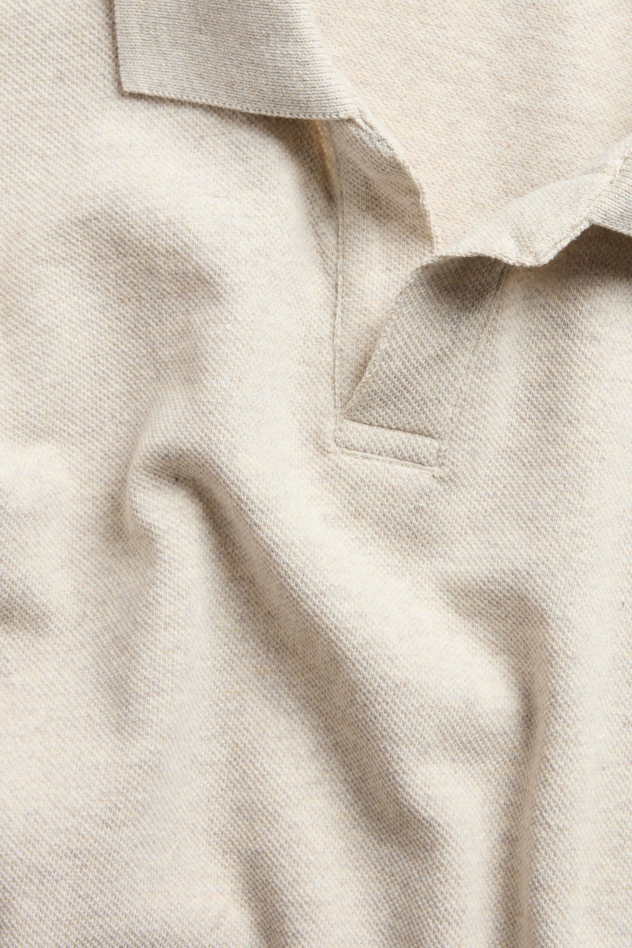 Nærbilde av en beigefarget melert piqué poloskjorte med krage og V-hals.